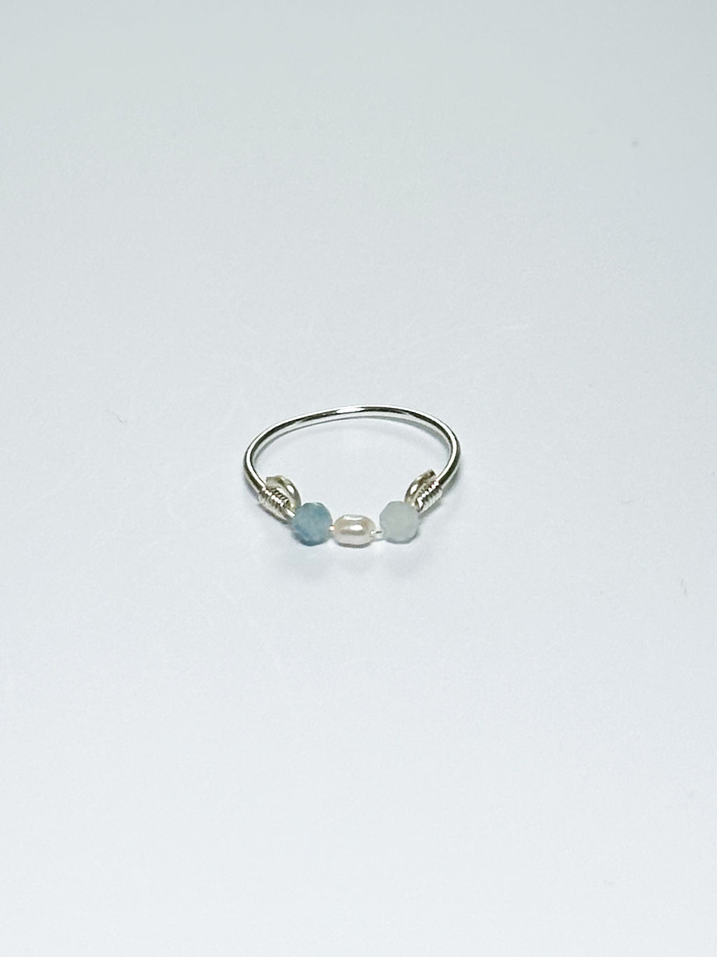 Silver wrapped Ring with Pearl in the middle and two light blue beads on two sides on a white background.