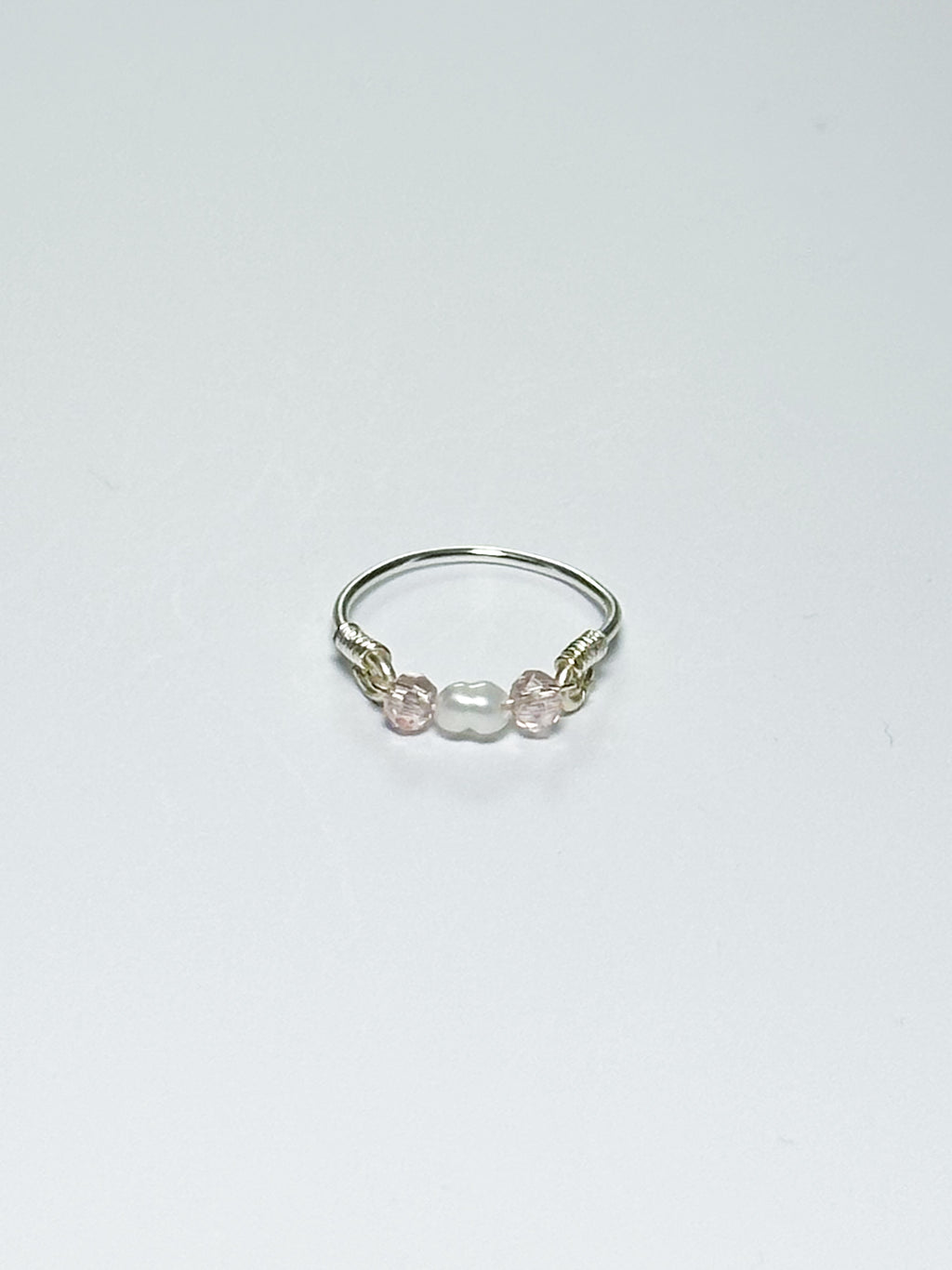 Silver wrapped Ring with Pearl in the middle and two pink beads on two sides on a white background.