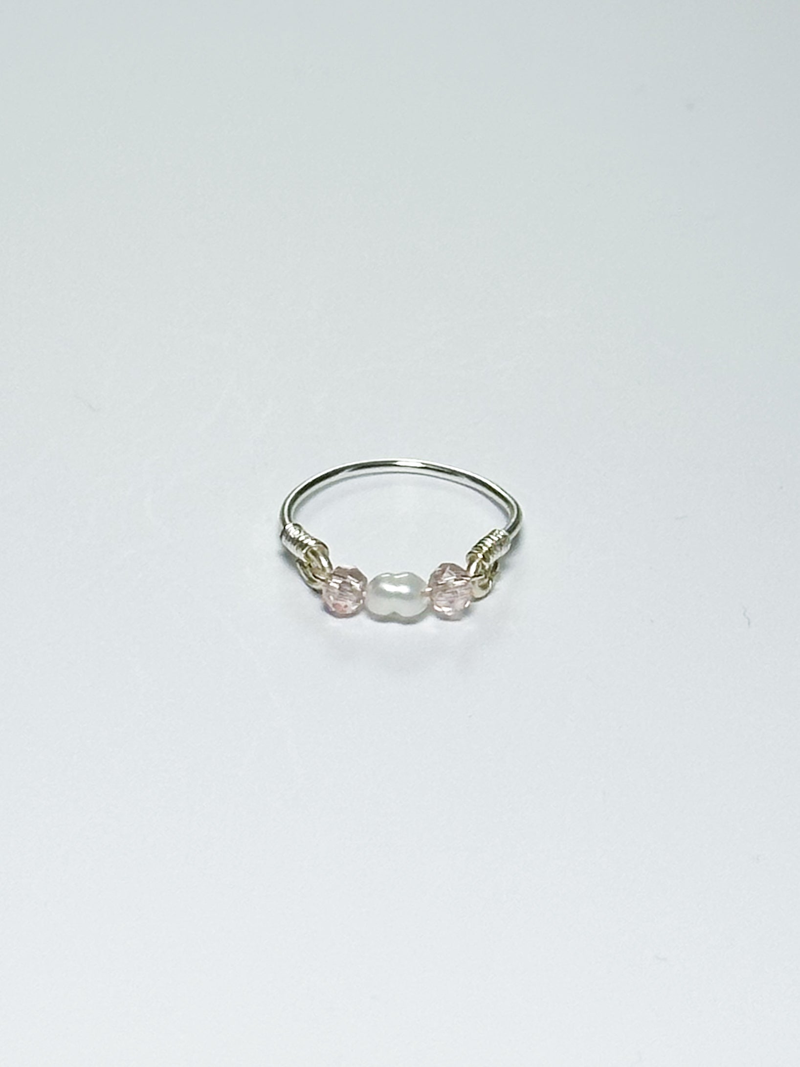Silver wrapped Ring with Pearl in the middle and two pink beads on two sides on a white background.