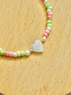 A close up half shot of a heart-shaped mother of pearl bracelet with colourful (pink, green and beige) beads on a wooden coaster.
