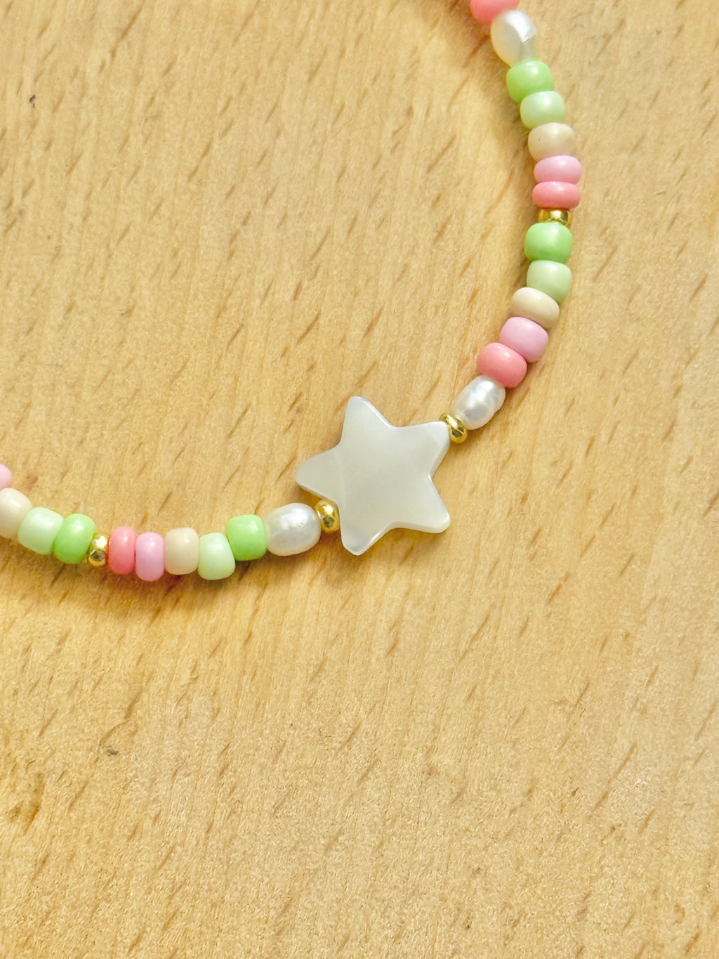 A close up half shot of a star-shaped mother of pearl bracelet with colourful (pink, green and beige) beads on a wooden coaster.