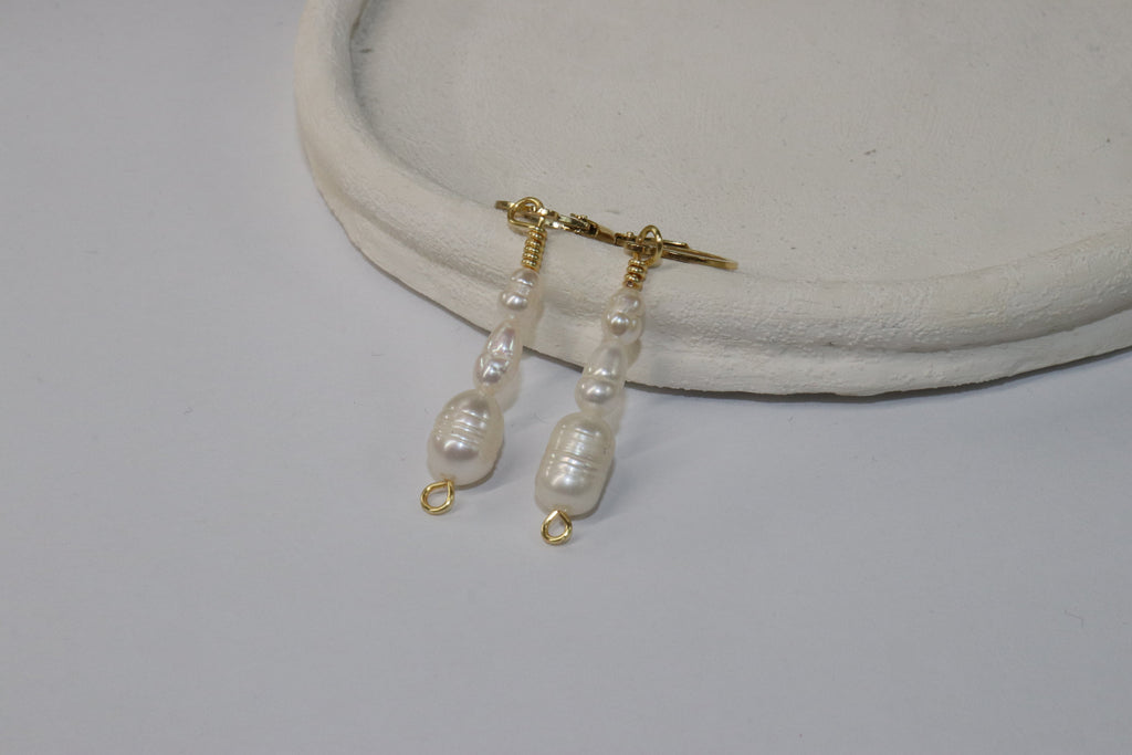 Cascade Gold Pearl Earrings with gold locks on a white surface. The body has three body pearls that get gradually bigger going down.