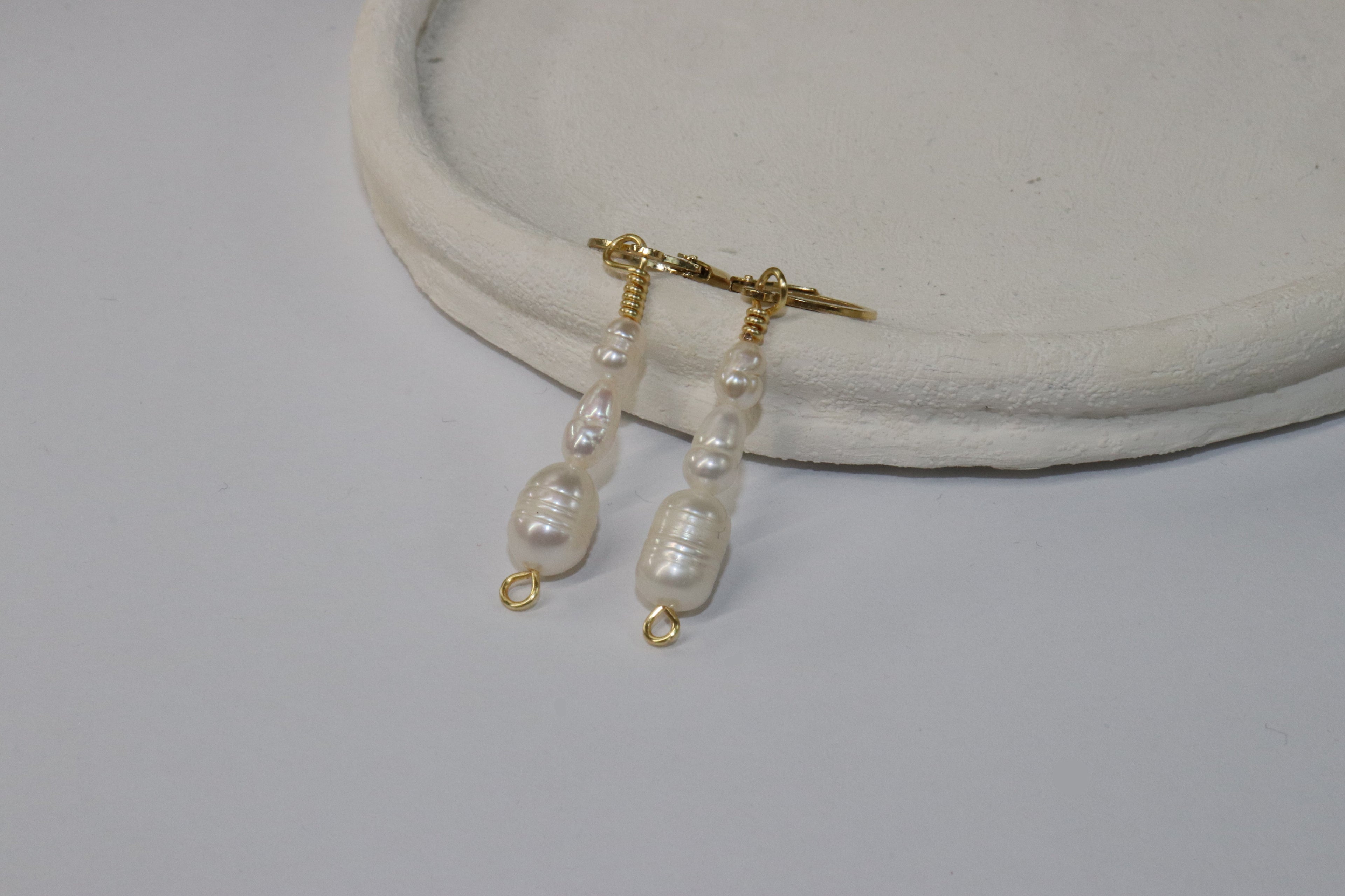 Cascade Gold Pearl Earrings with gold locks on a white surface. The body has three body pearls that get gradually bigger going down.