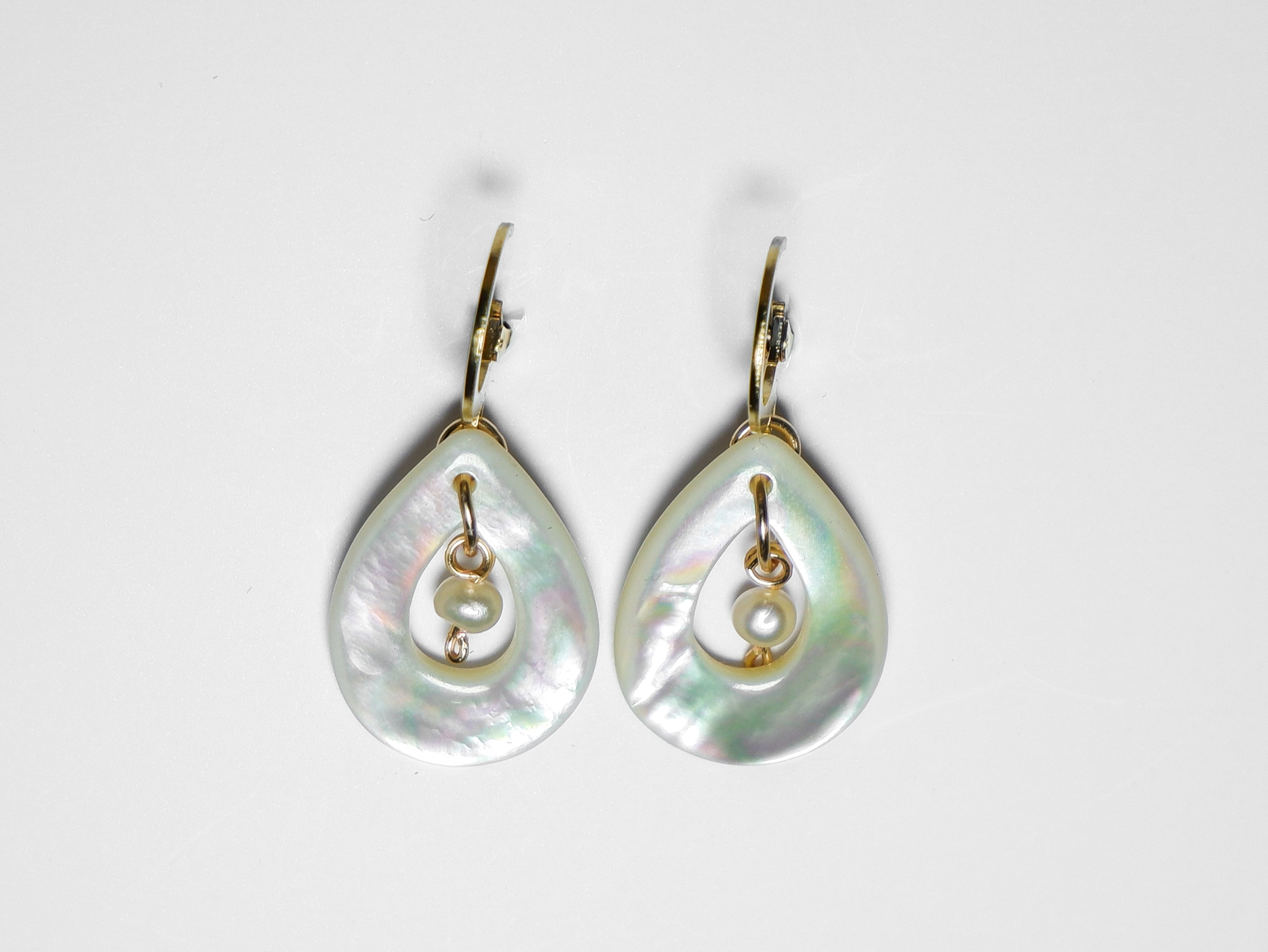 A close-up horizontal shot of gold earrings with teardrop-shaped mother of pearl with pearl in the middle on a white background.