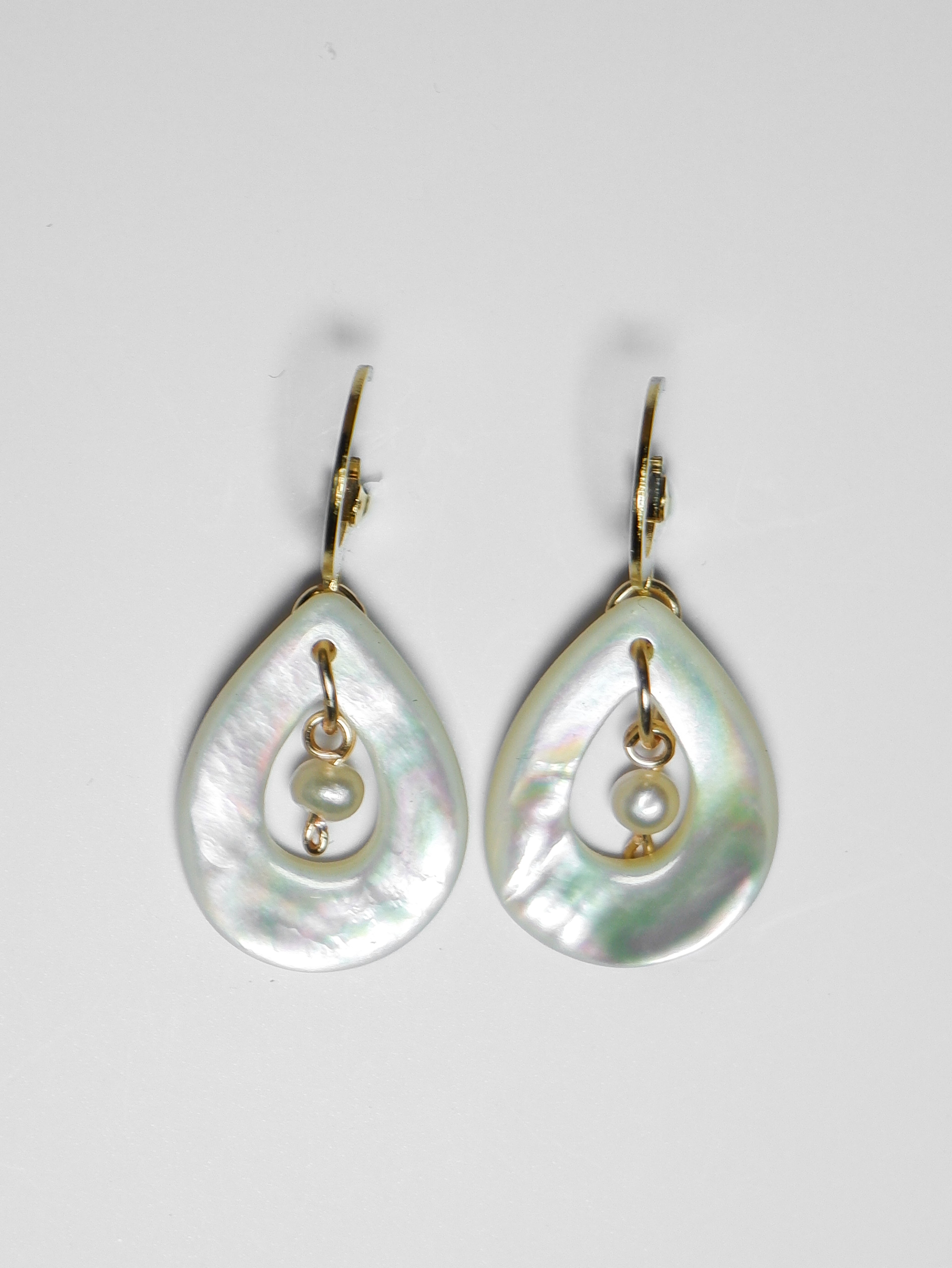 A close-up shot of gold earrings with teardrop-shaped mother of pearl with pearl in the middle on a white background.