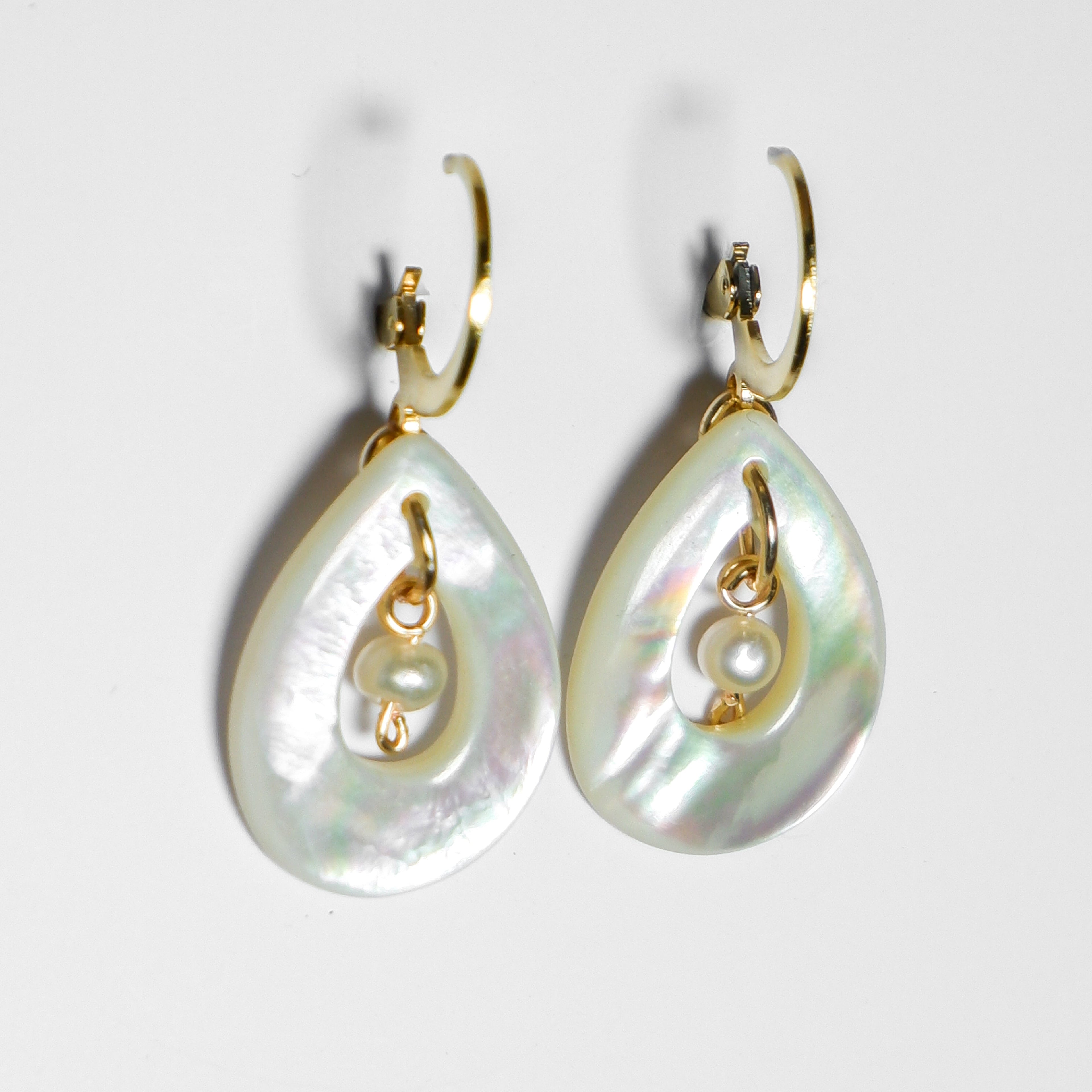 An ultra-close up side shot of gold earrings with teardrop-shaped mother of pearl with pearl in the middle on a white background.