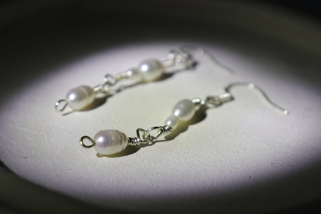 Pearl link silver earrings on a dark background with a spotlight effect, with zoomed effects detailing the hooks and pearls of one of the earrings