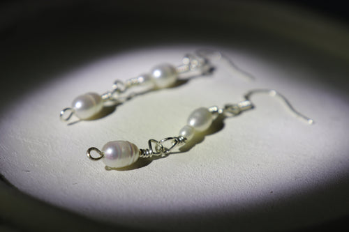Pearl link silver earrings on a dark background with a spotlight effect, with zoomed effects detailing the hooks and pearls of one of the earrings
