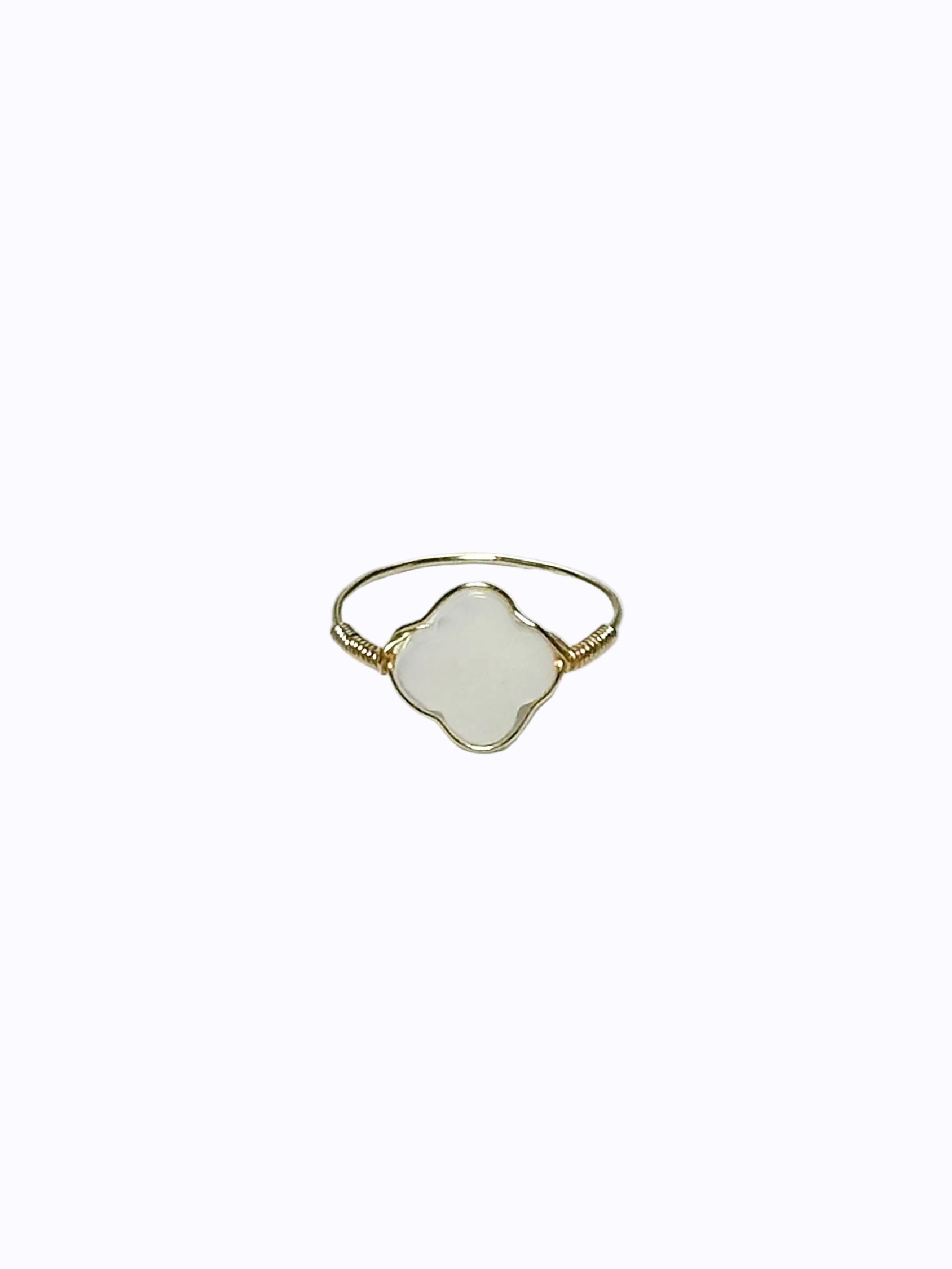 Gold wrapped ring with clover-shaped mother of pearl in the middle on a white background.