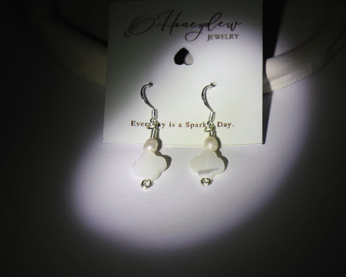 Pair of silver earrings, Made from Mother of pearls and pearls, with a clover design on a 'Honeydew Jewellery' packaging.  Stage light is shining on them on a dark background.