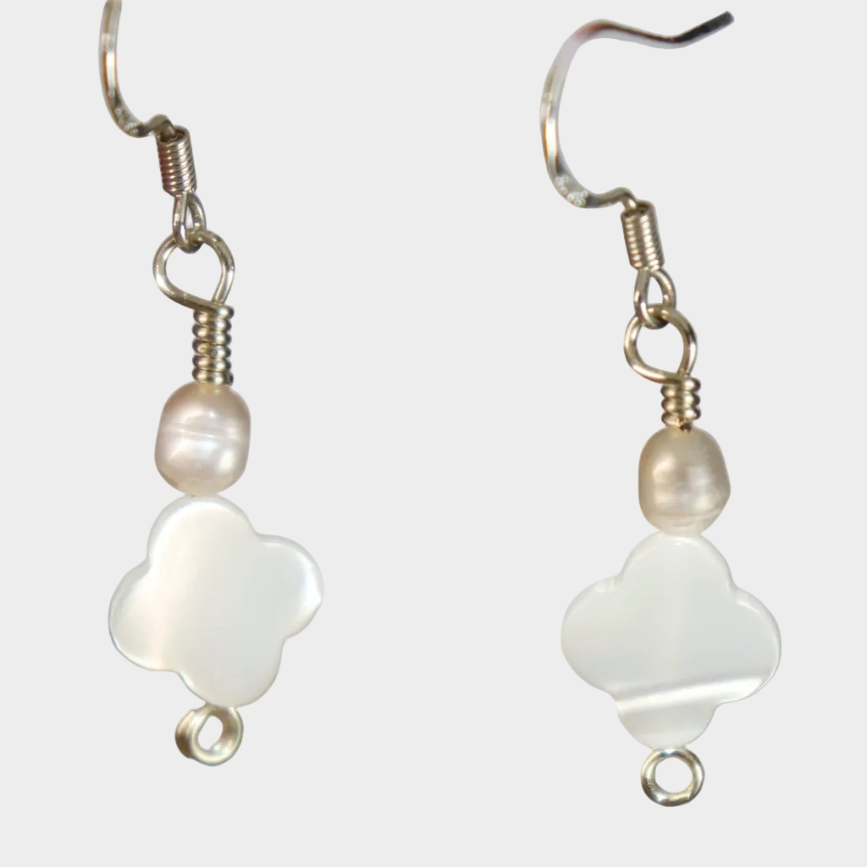 Pair of silver earrings with white clover designs made from mother of pearl and pearl on a white-ish background.