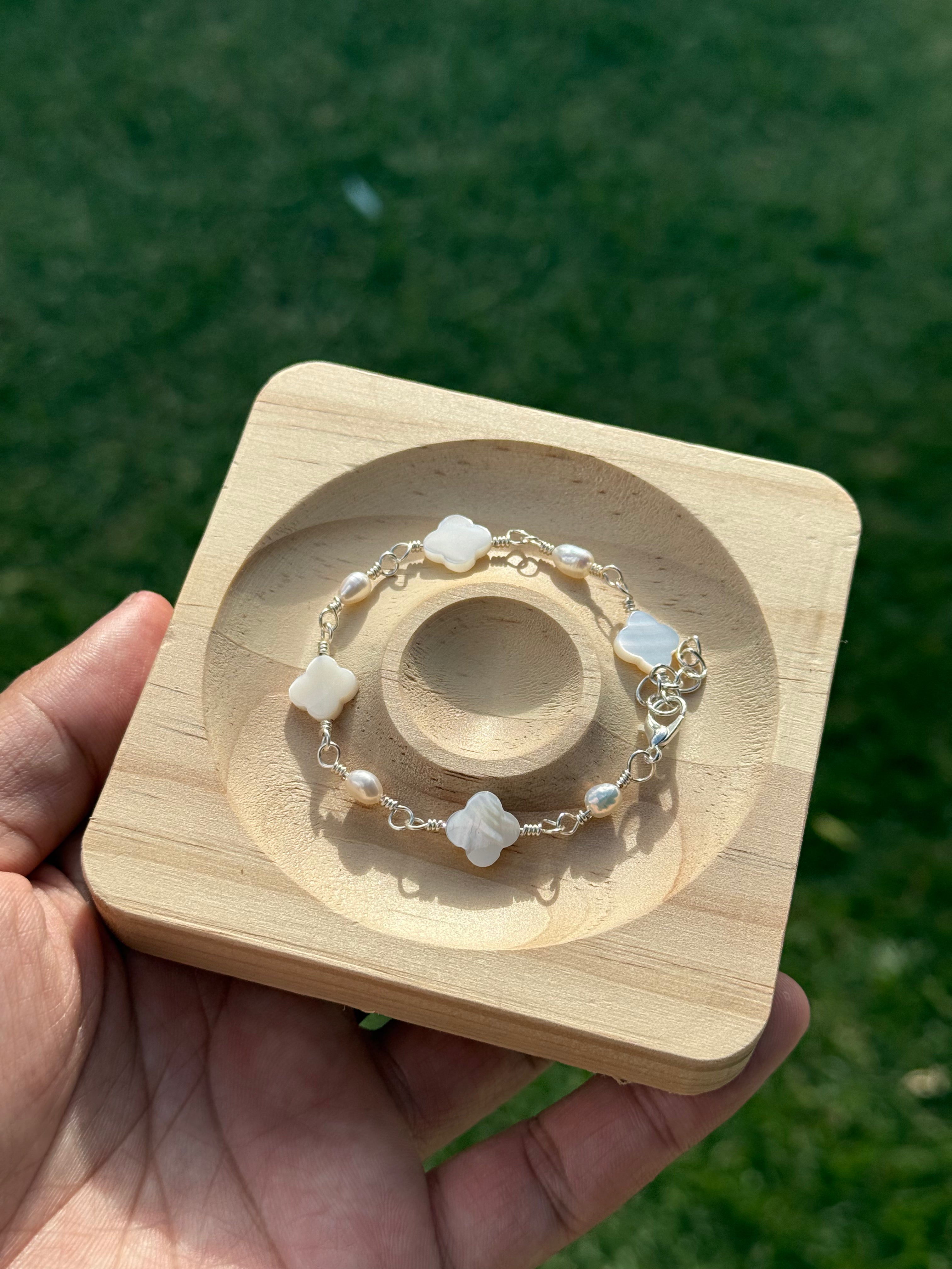 Silver Clover Pearl and Mother of Pearl Bracelet on a display tray held by a hand against a green grass outdoor background.