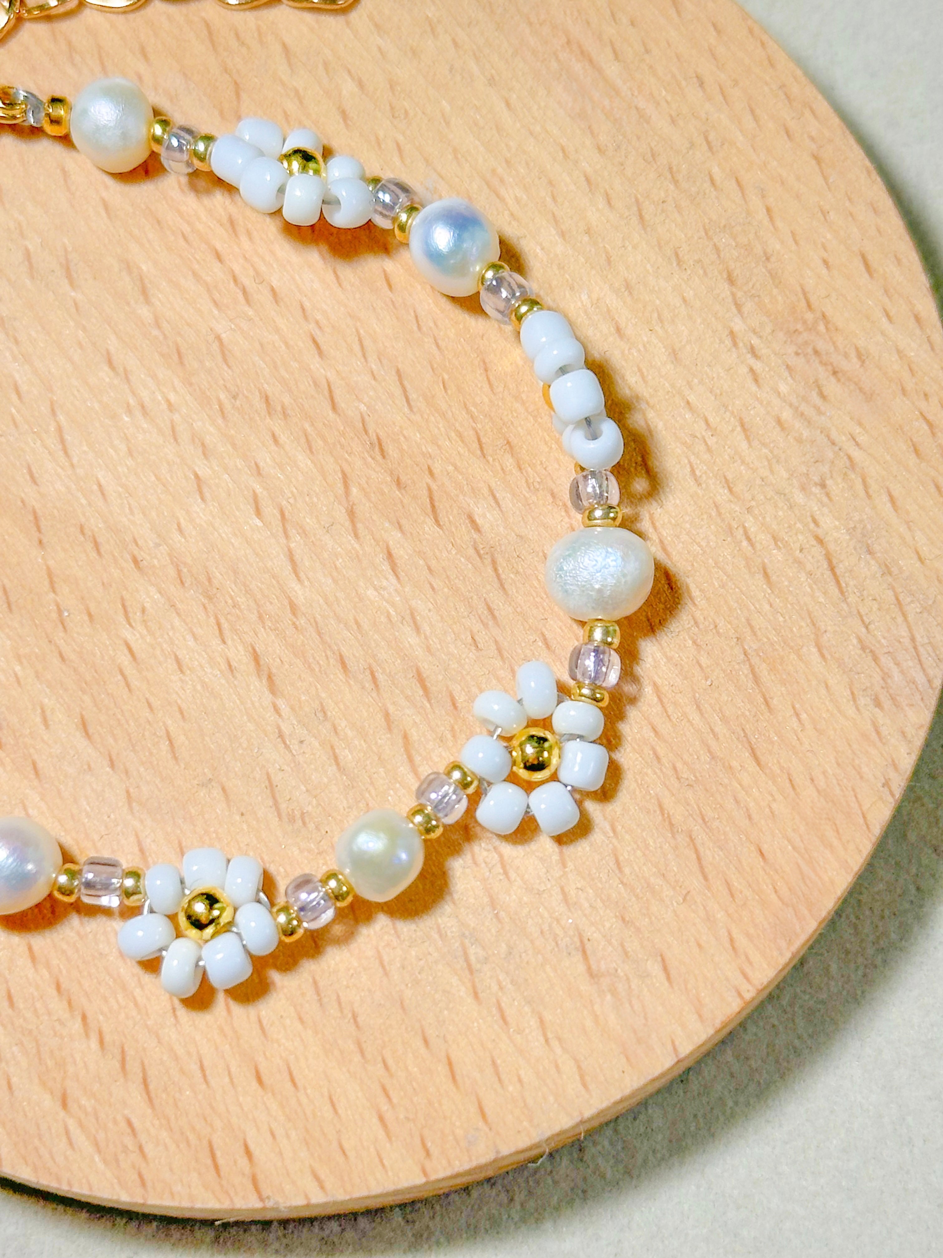 Daisy Bracelet with handmade daisy flowers with beads, some pearls, and  gold accents on a wooden surface.