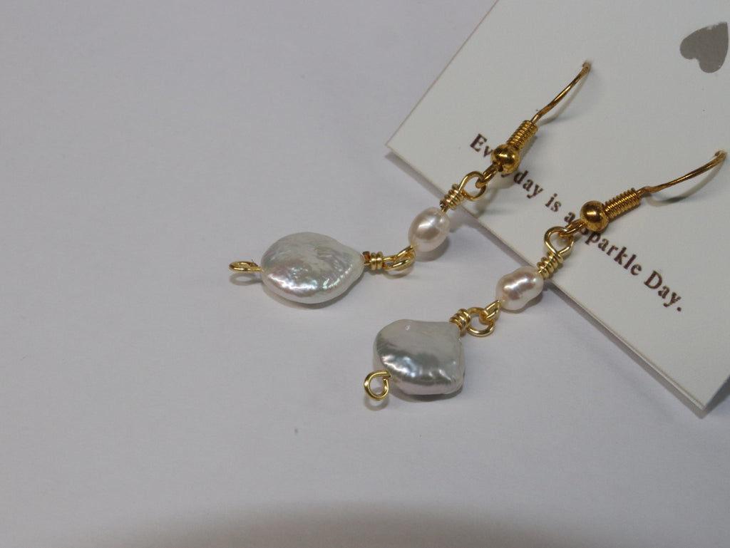 A close up shot of Gold link earrings with pill-shaped pearl and round, plate-shaped pearl, on a white card with Honeydew's slogan "Everyday is a Sparkle Day" with white background.