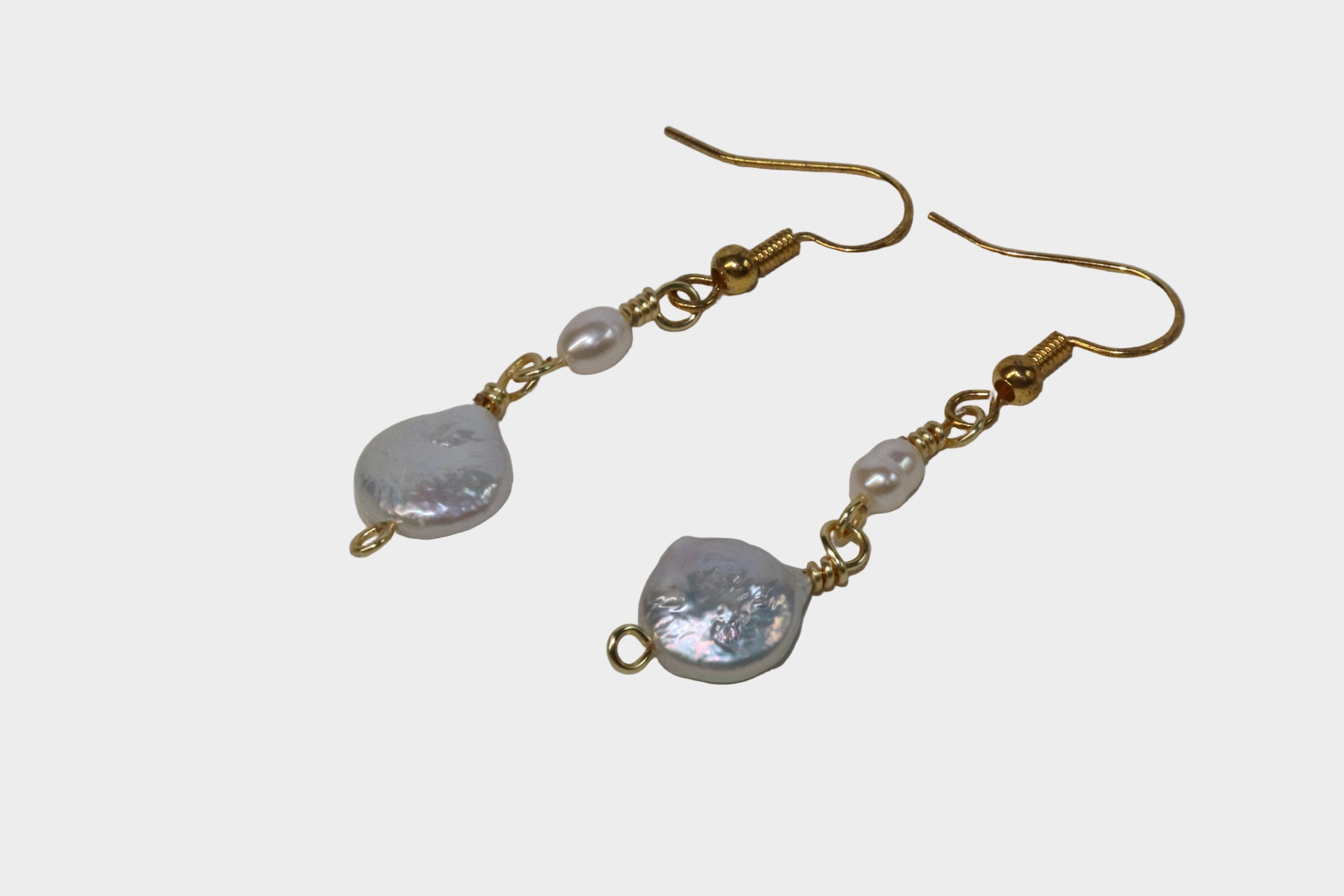 Pair of gold pearl earrings with gold hooks on a white background.