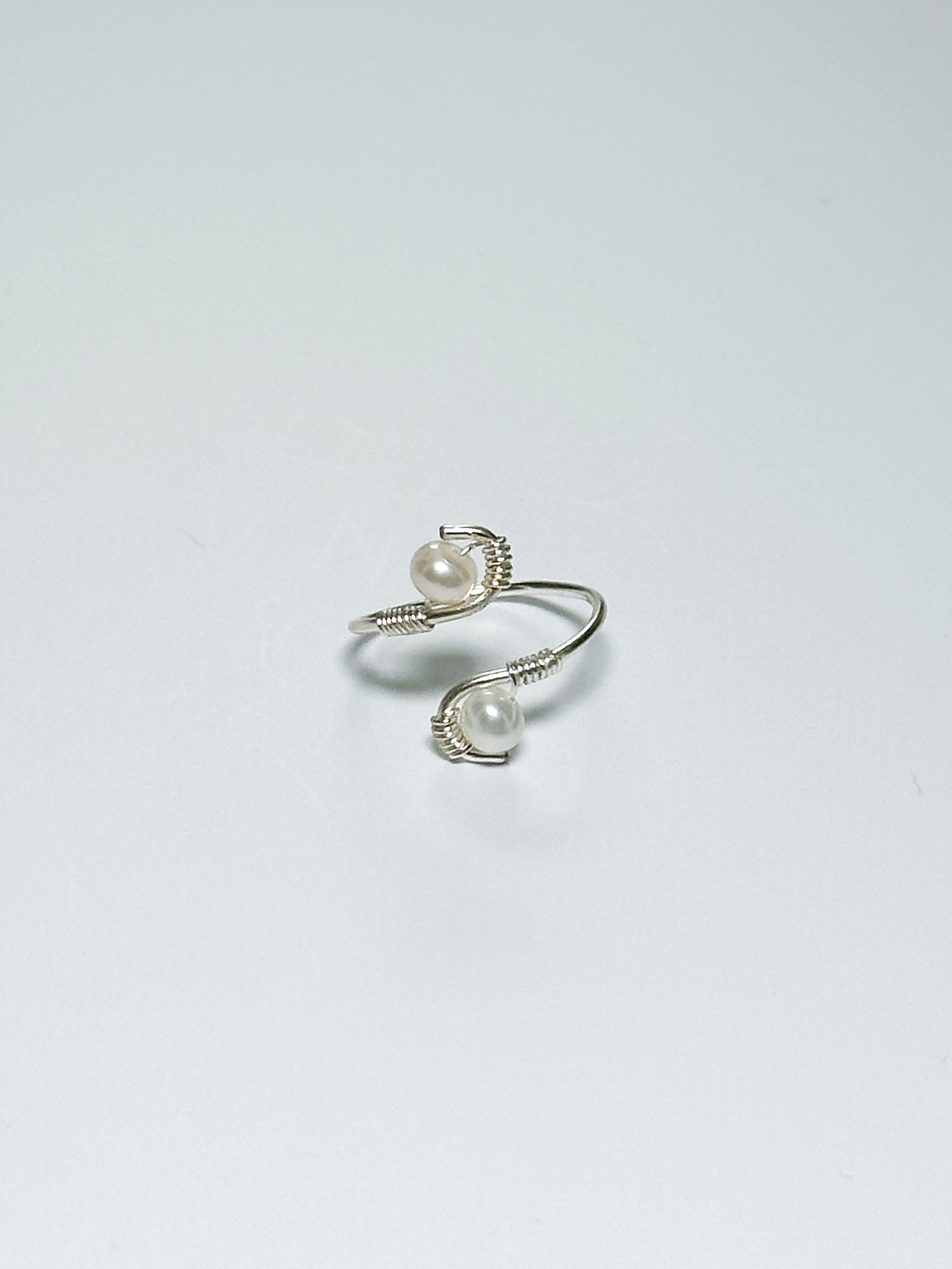 A silver pearl ring with a by-pass style body, creating an S-like body on a white background and shadow.