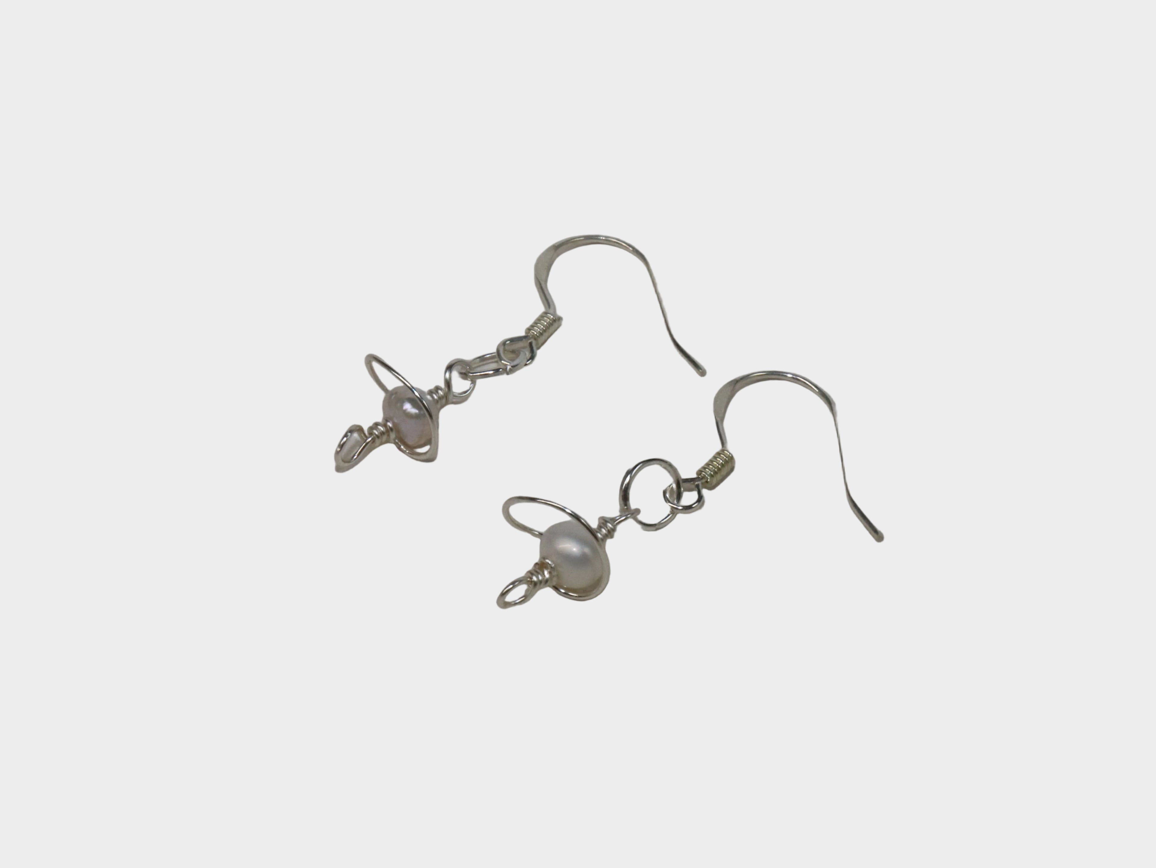 Laying down Silver pearl earrings with a galaxy-like body design on a white background.