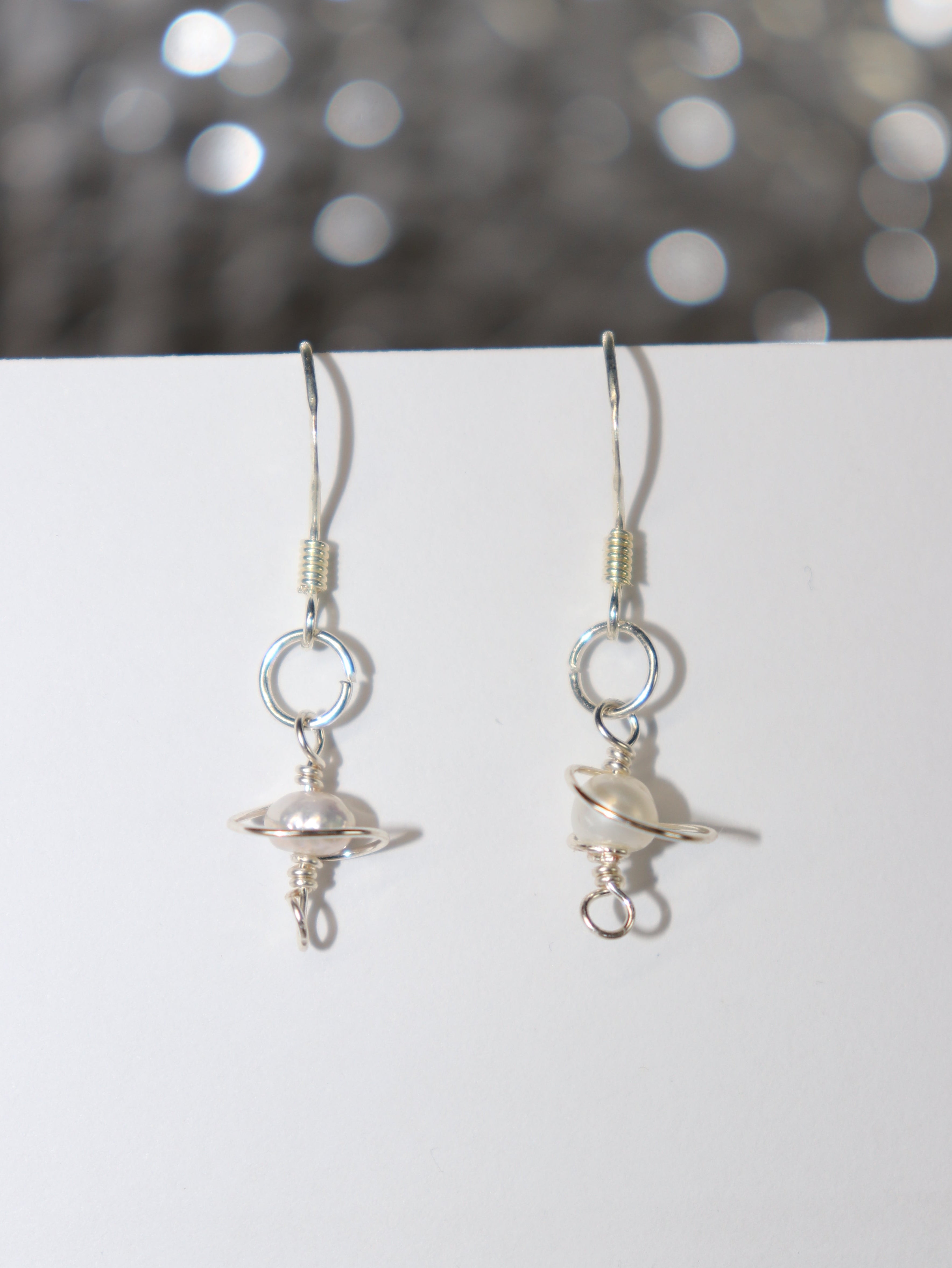 Silver earrings with a galaxy-like body with pearls on a white surface with a blurred background.