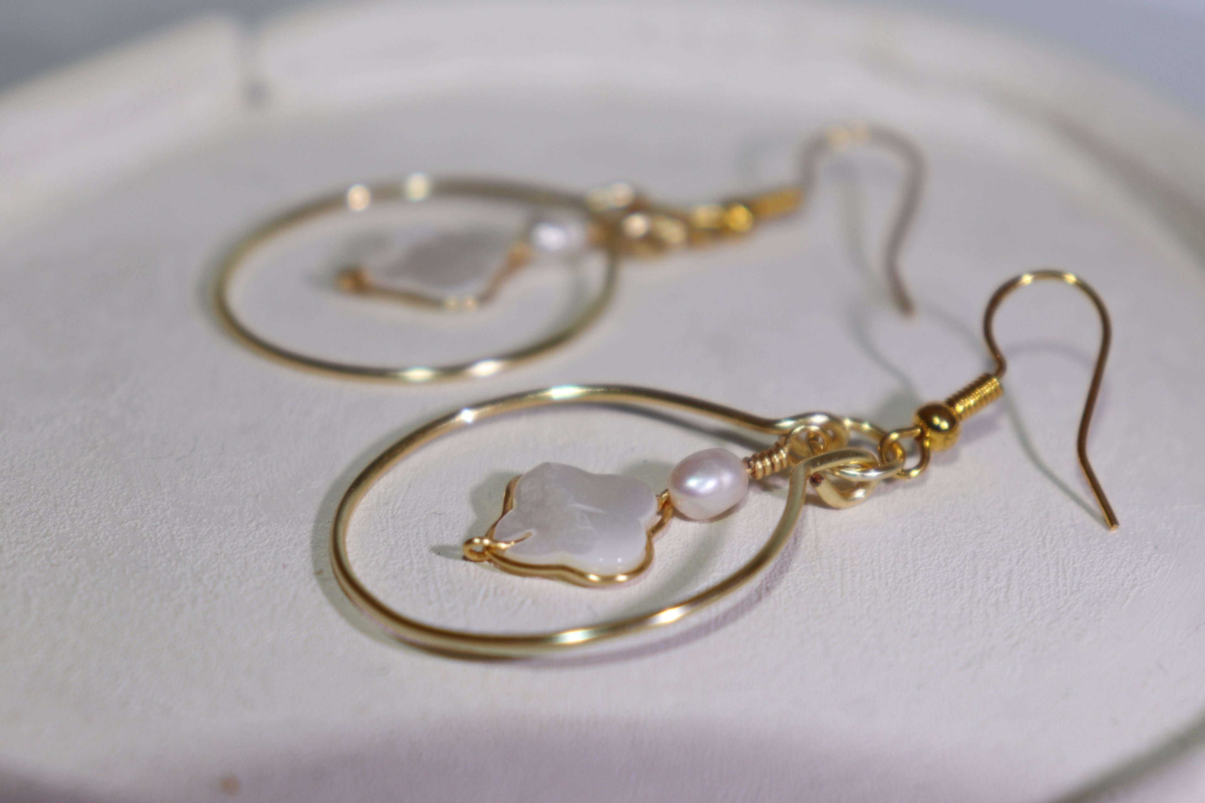 Handmade gold hoop mother of pearl earrings with freshwater pearl on a white clay plate.