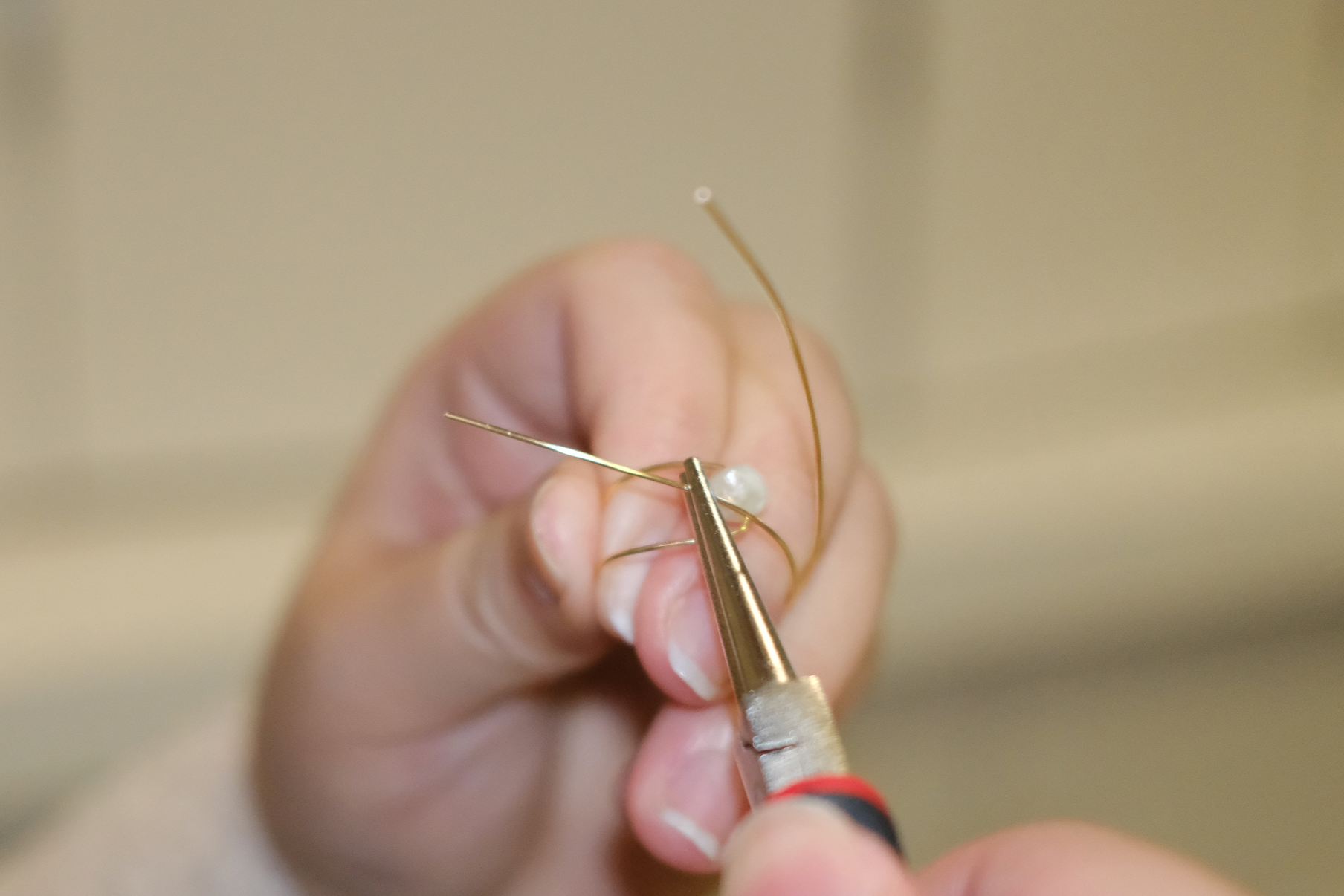 Close-up of hands of Zoey, the co-founder, using a tool to wrap a pearl  ring, with blurred, neutral background.