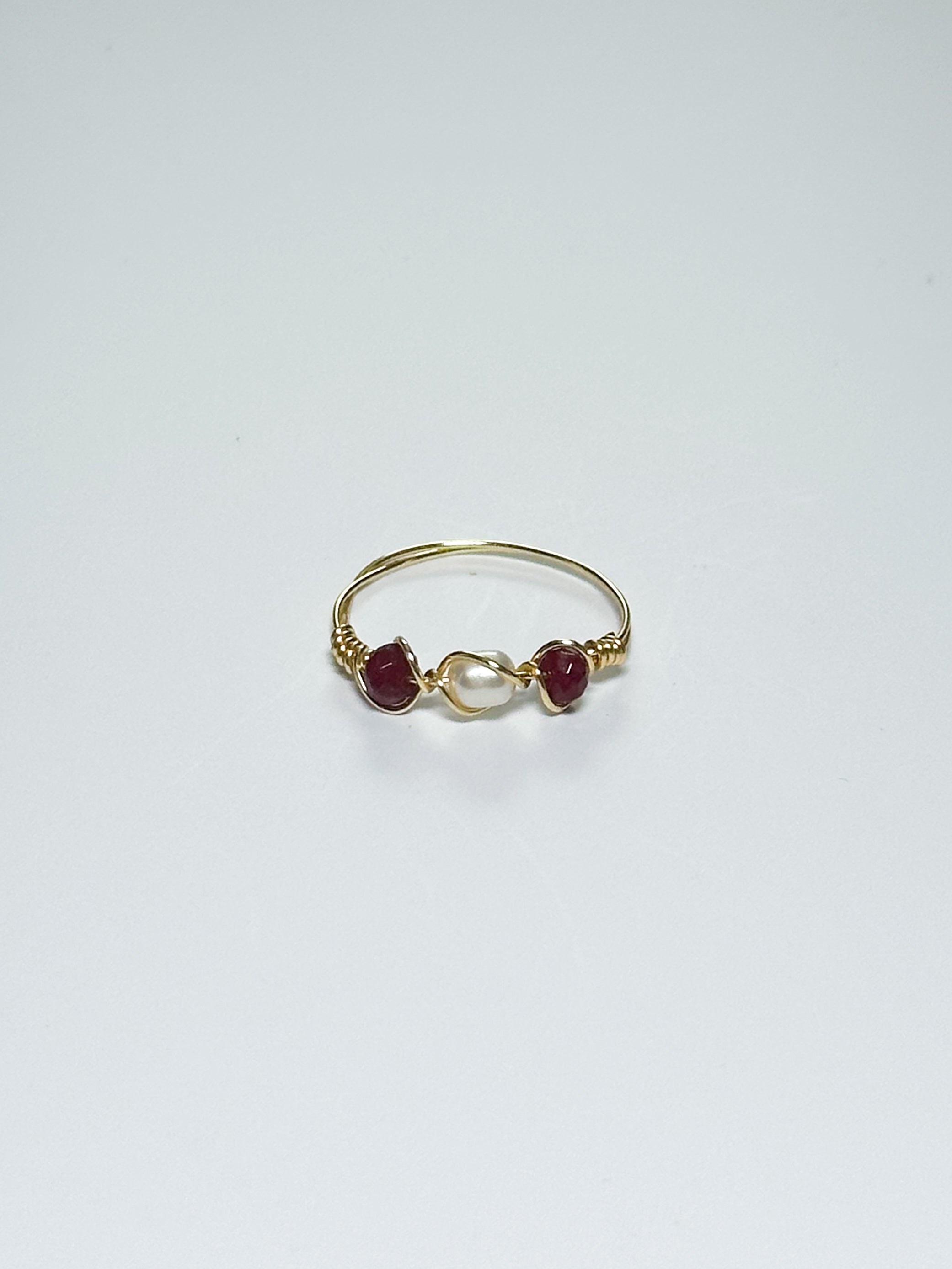 Gold Wrapped Ring with Pearl in the middle and two crimson red beads on two sides on a white background.