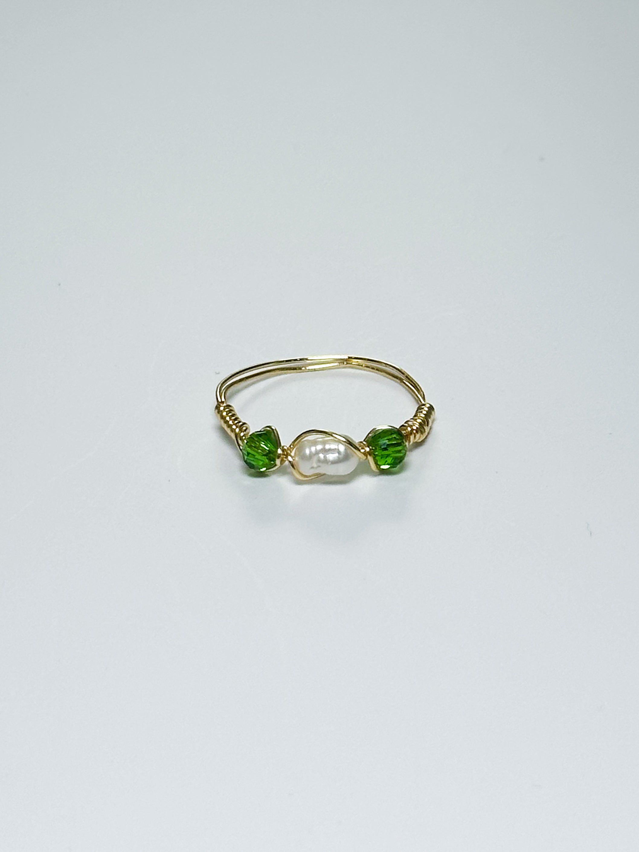 Gold Wrapped Ring with Pearl in the middle and two green beads on two sides on a white background.