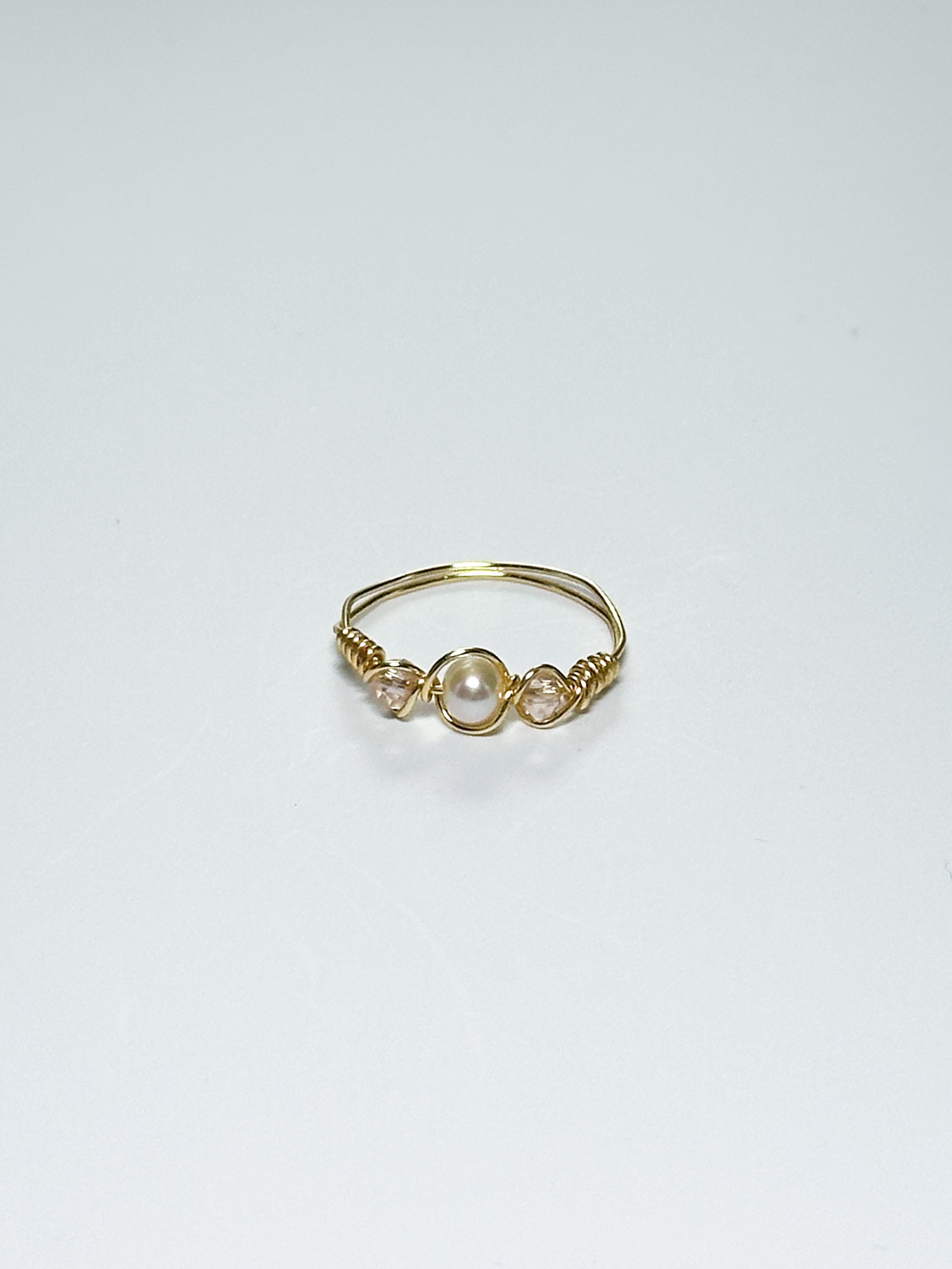 Gold Wrapped Ring with Pearl in the middle and two pink beads on two sides on a white background.