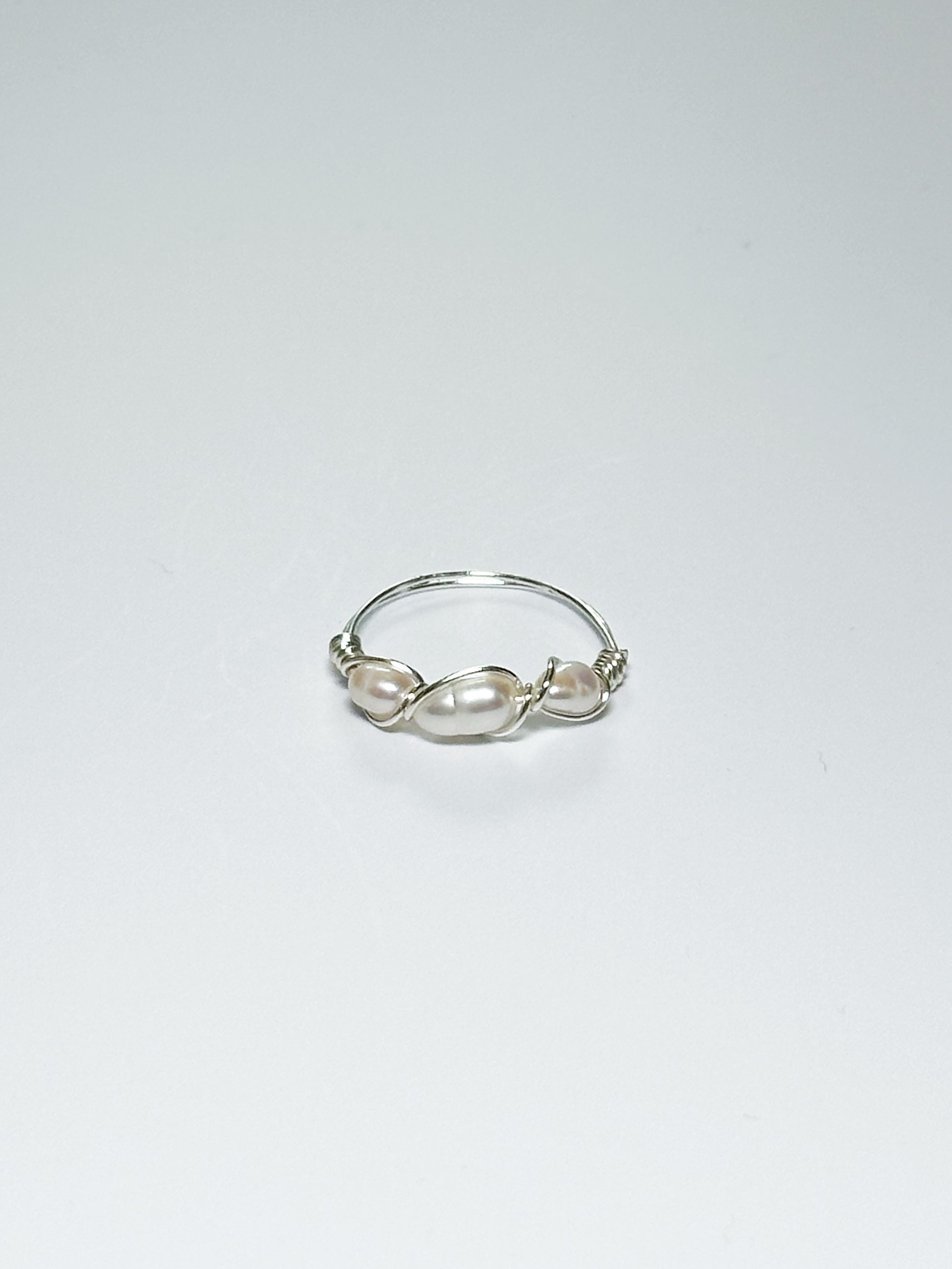 Silver Wrapped Ring with three Pearls in the middle on a white background with shadows.