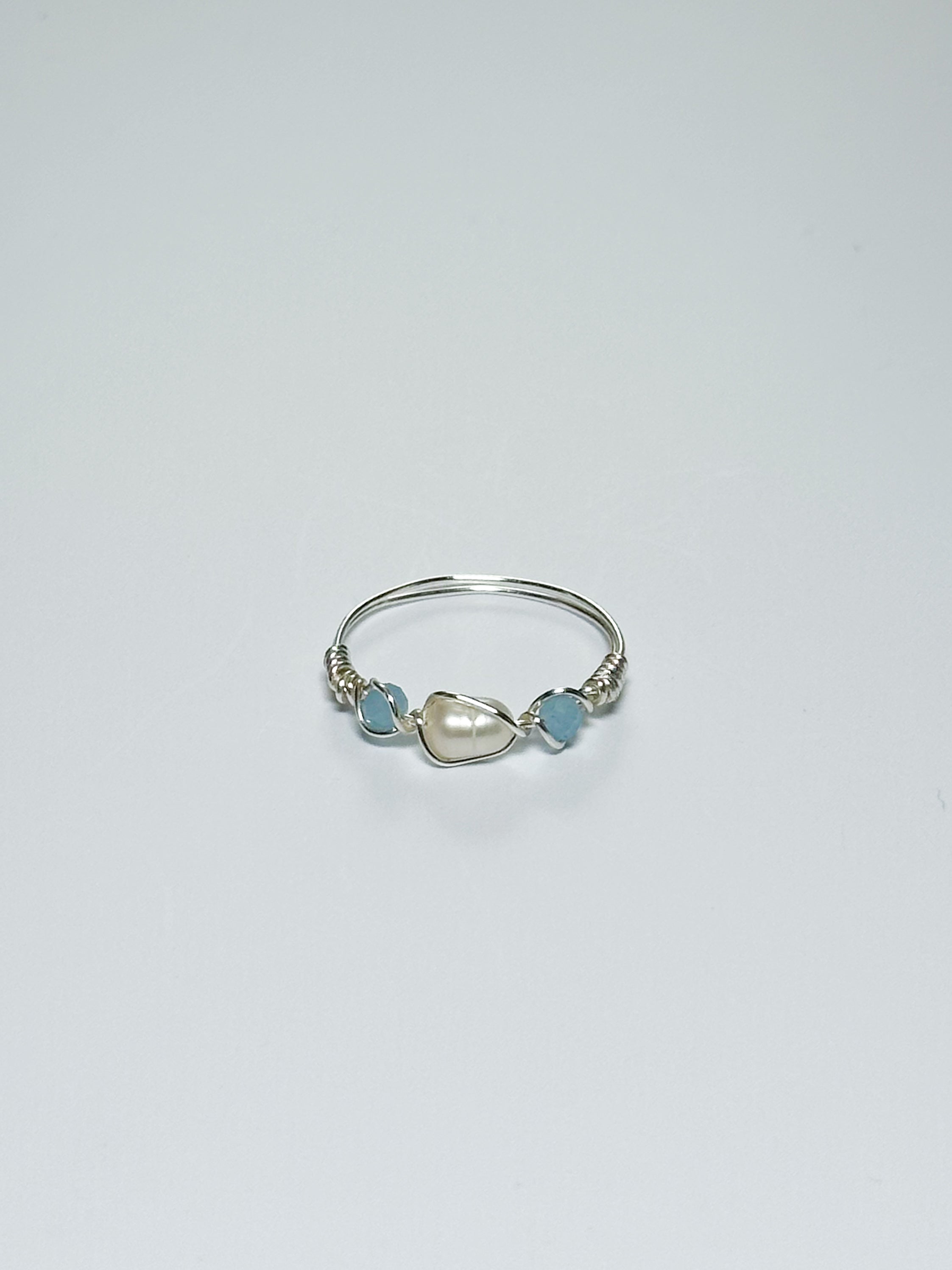Silver wrapped ring with a pearl and two sky blue beads on two sides on a white background.