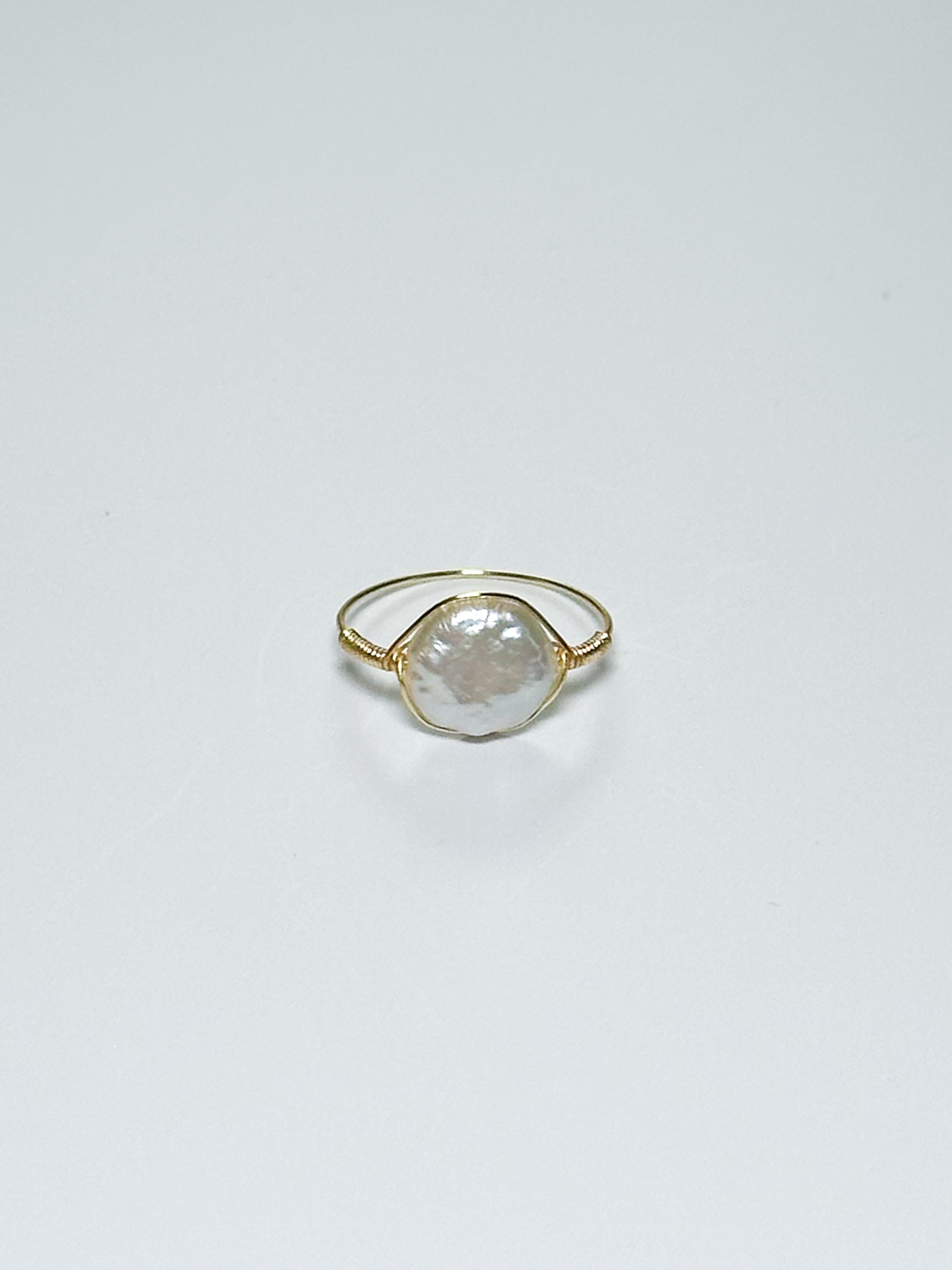 Gold wrapped ring with an oval-shaped pearl in the middle on white background with shadows.