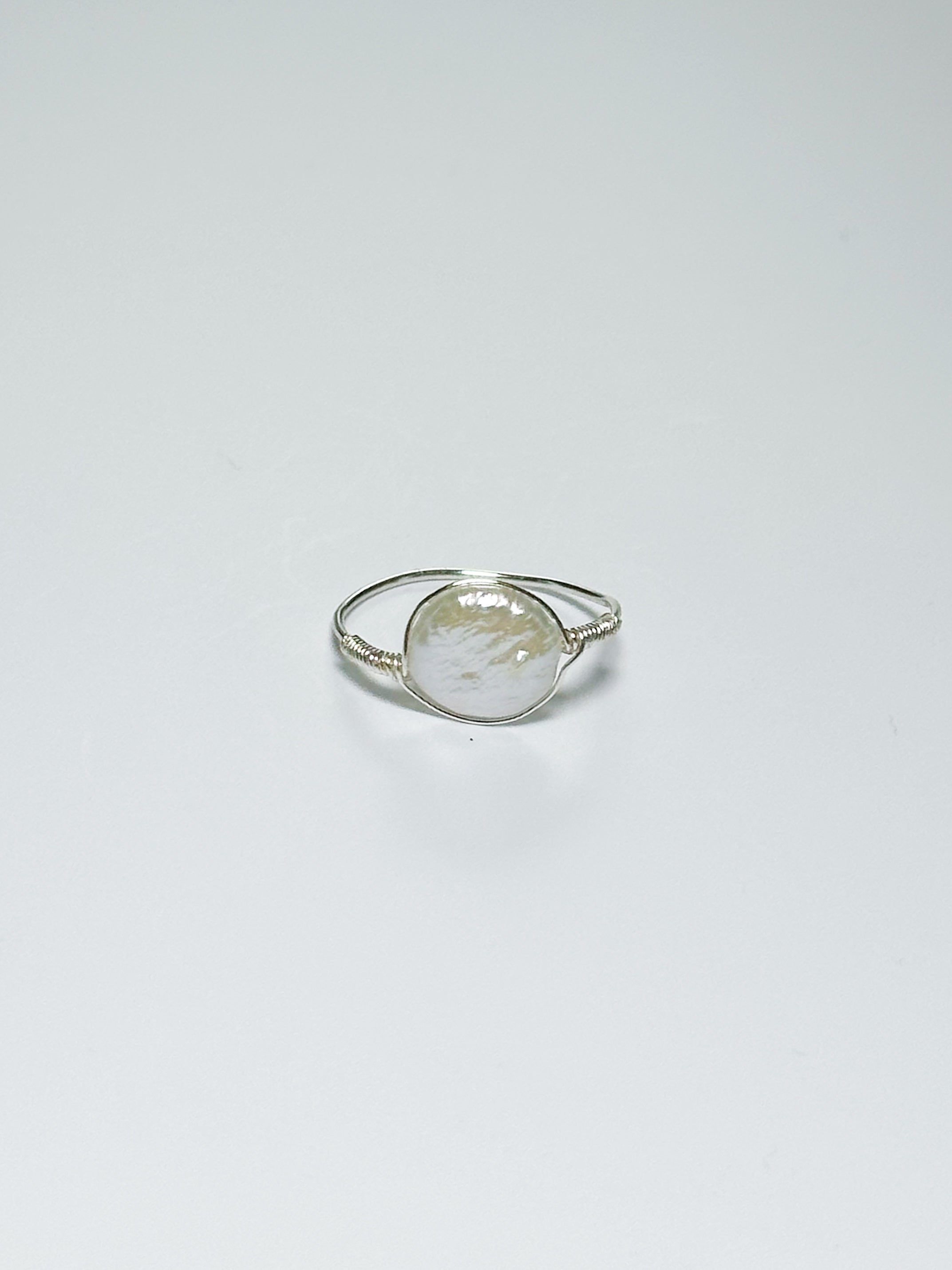 A silver wrapped ring with oval-shaped pearl in the middle on a white background with shadows.