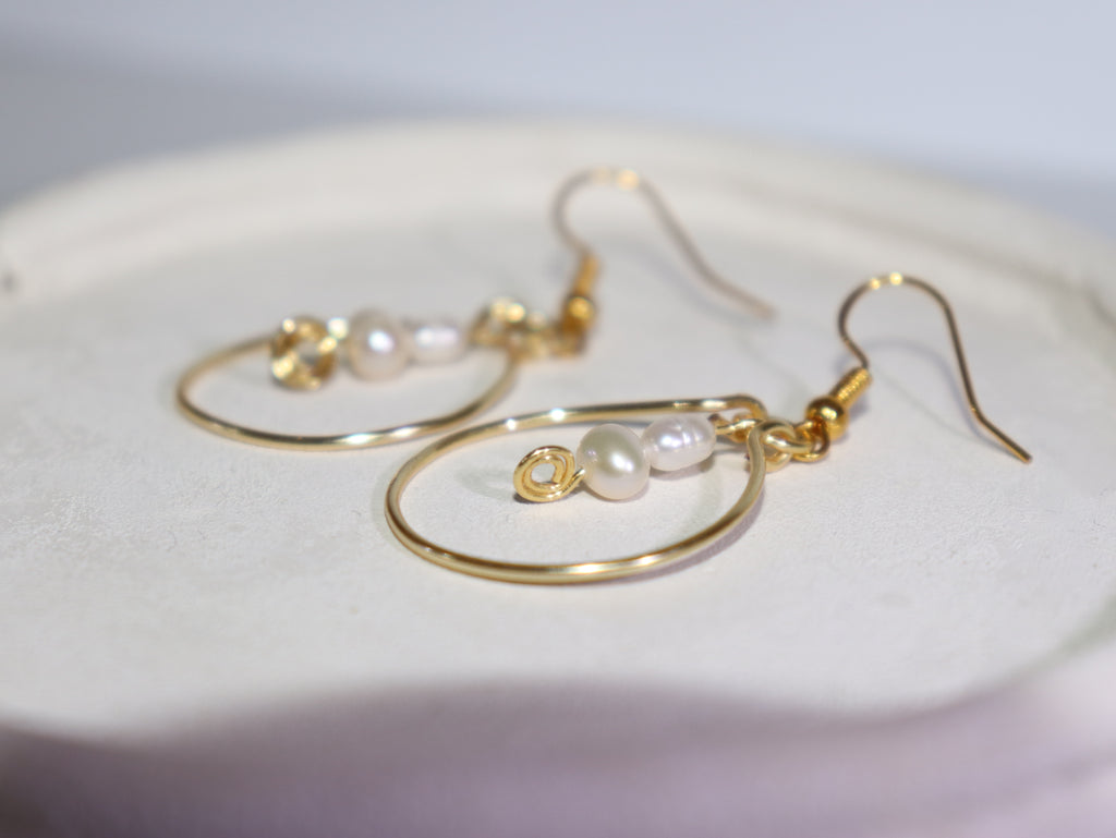 Gold hoop pearl earrings on a white light grey background.
