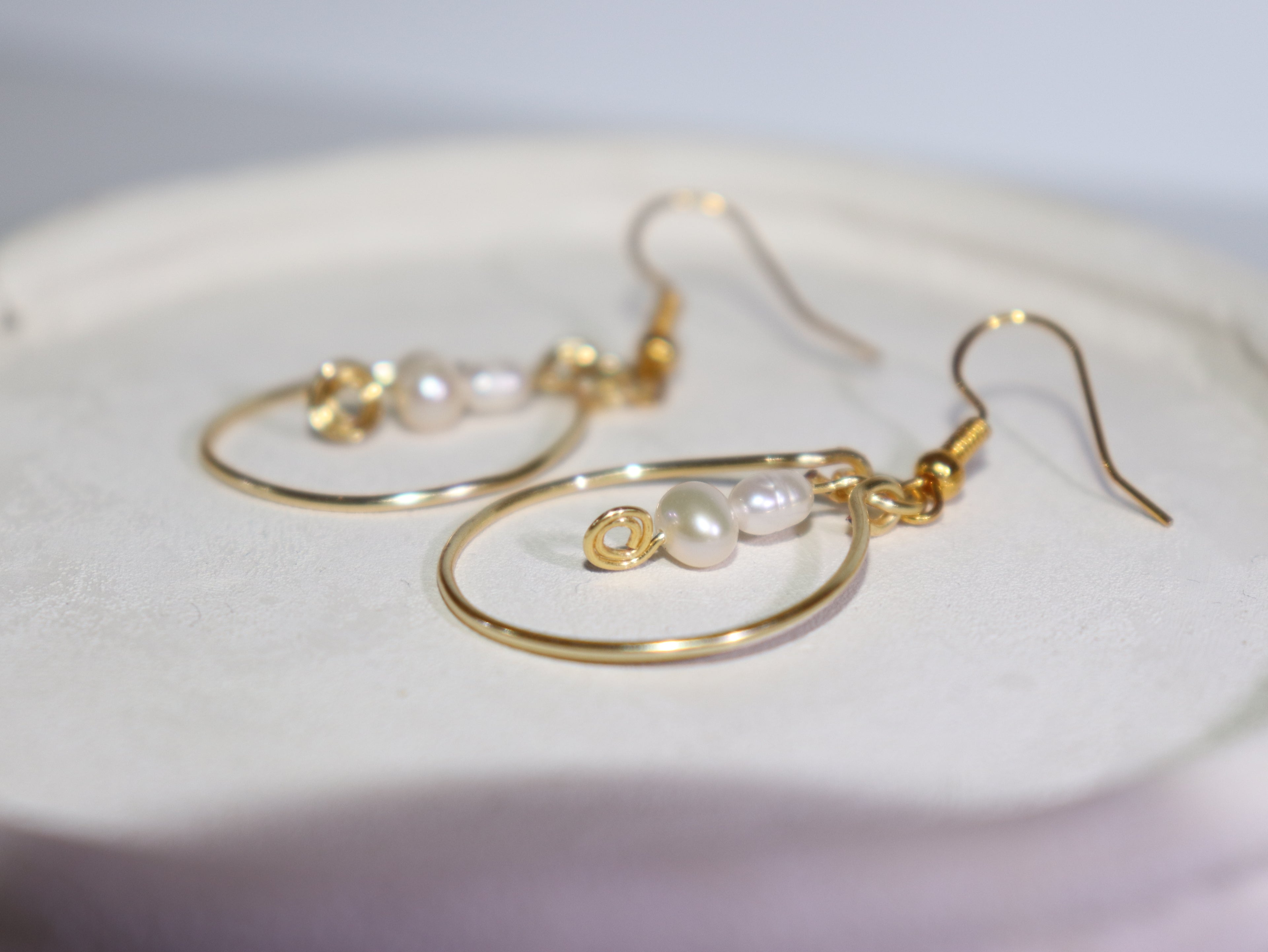 Gold hoop pearl earrings on a white light grey background.