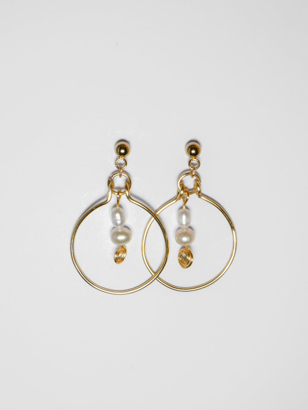 Gold hoop pearl earrings on a light grey background.