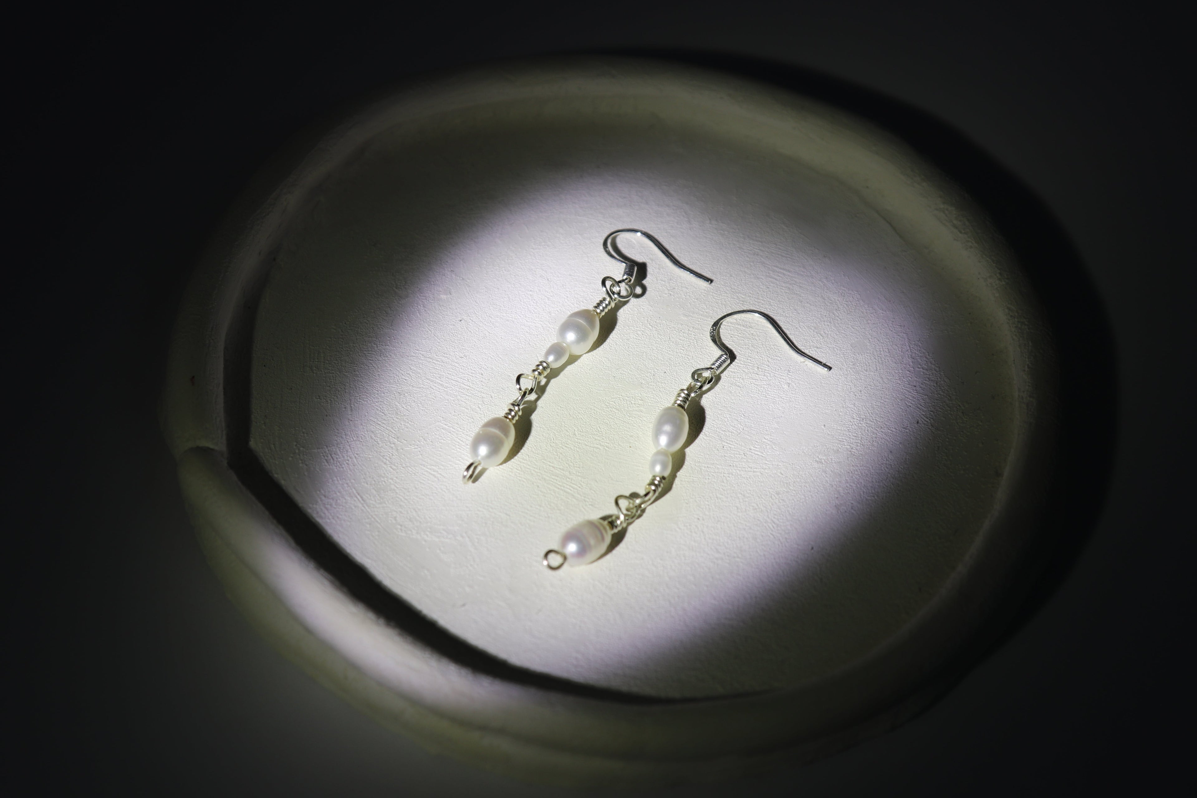 Pearl link earrings on a dark background with a spotlight effect