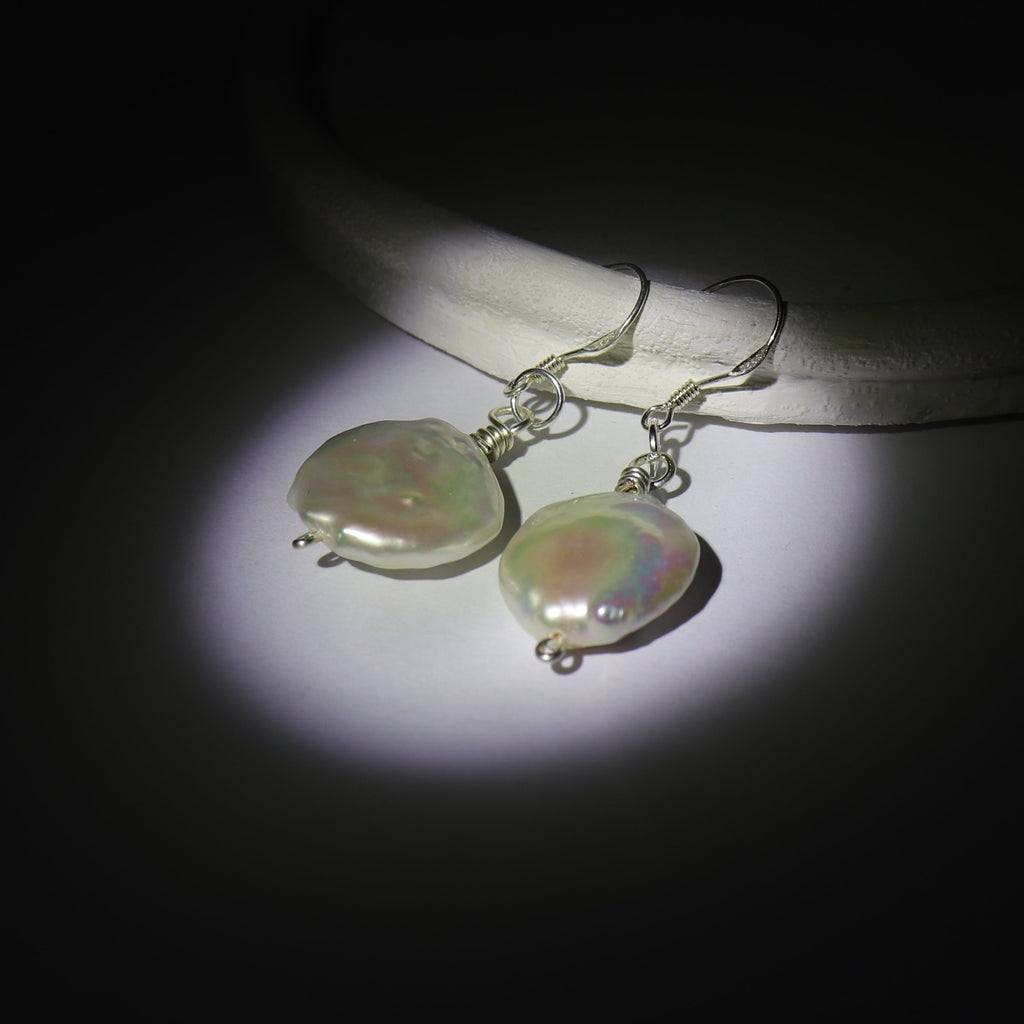 Large Round pearl earrings on a dark background. Using spotlight effect, the earrings has a pearlescent effect illuminating them.
