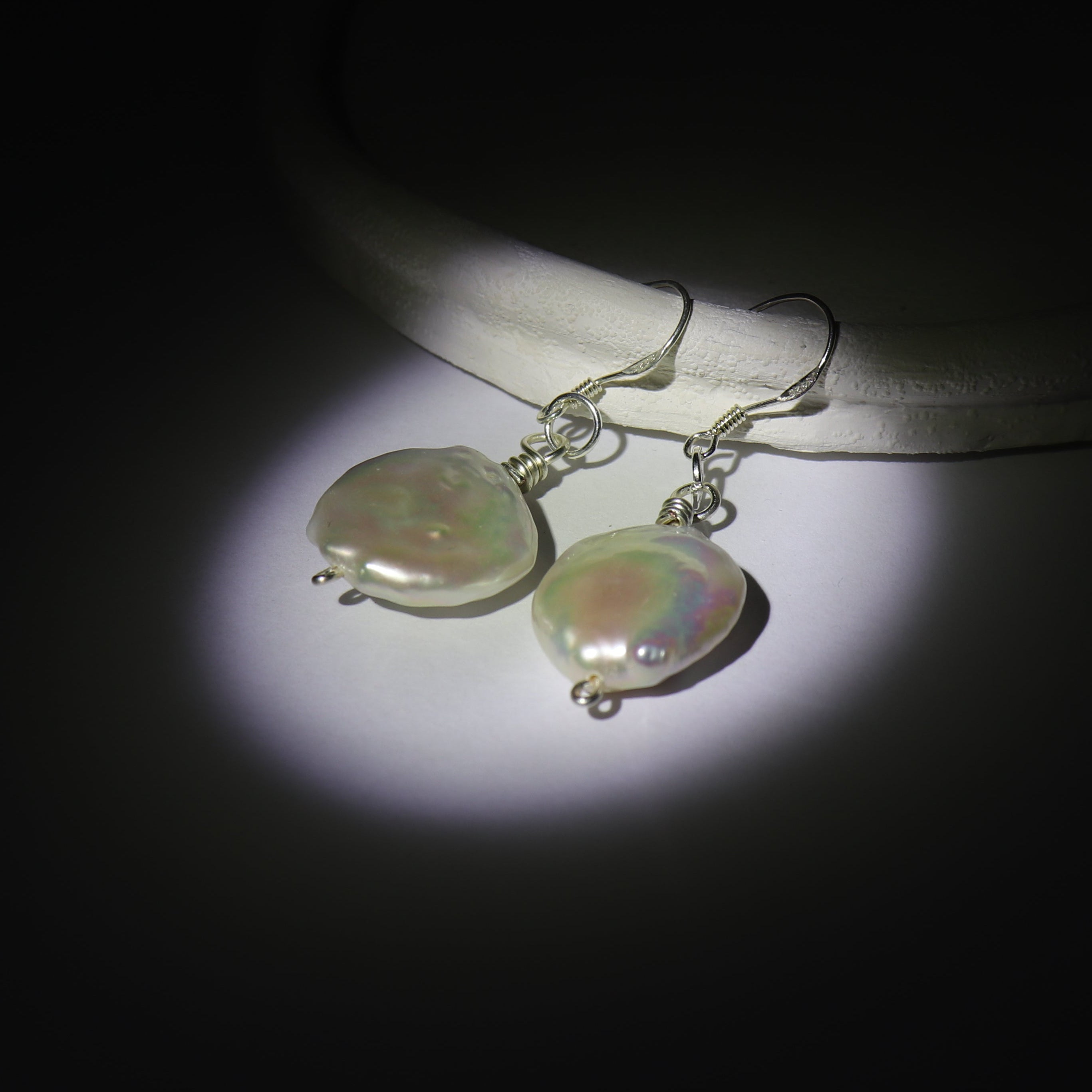 Large Round pearl earrings on a dark background. Using spotlight effect, the earrings has a pearlescent effect illuminating them.