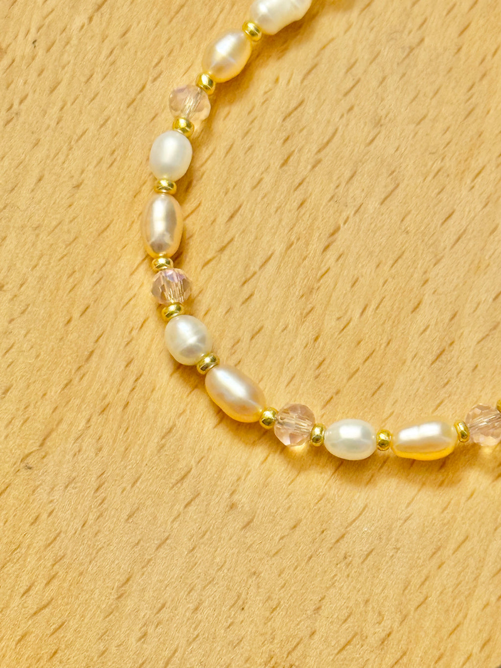 A close up half shot of a pearl, pink beads, and gold bracelet on a wooden coaster.