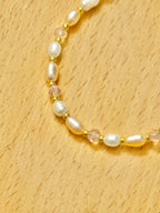 A close up half shot of a pearl, pink beads, and gold bracelet on a wooden coaster.