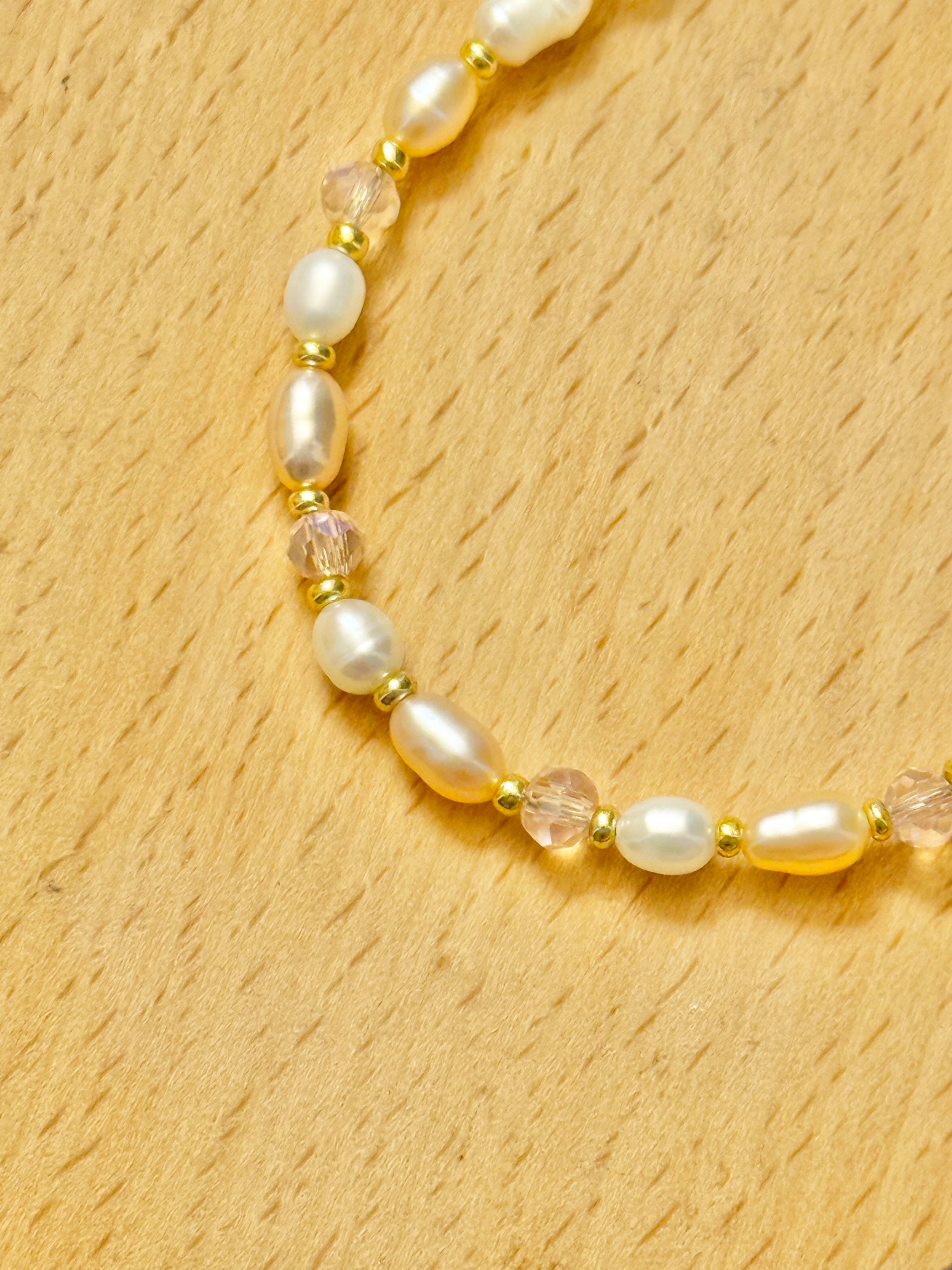 A close up half shot of a pearl, pink beads, and gold bracelet on a wooden coaster.