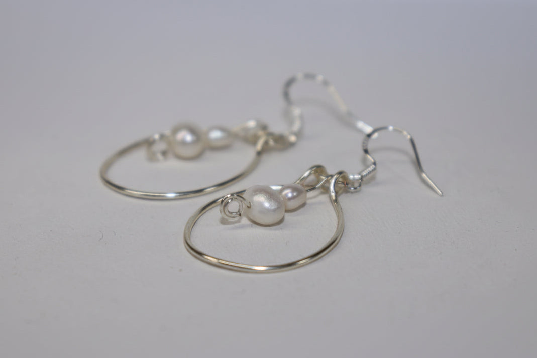 Silver hoop pearl earrings on a white light grey background