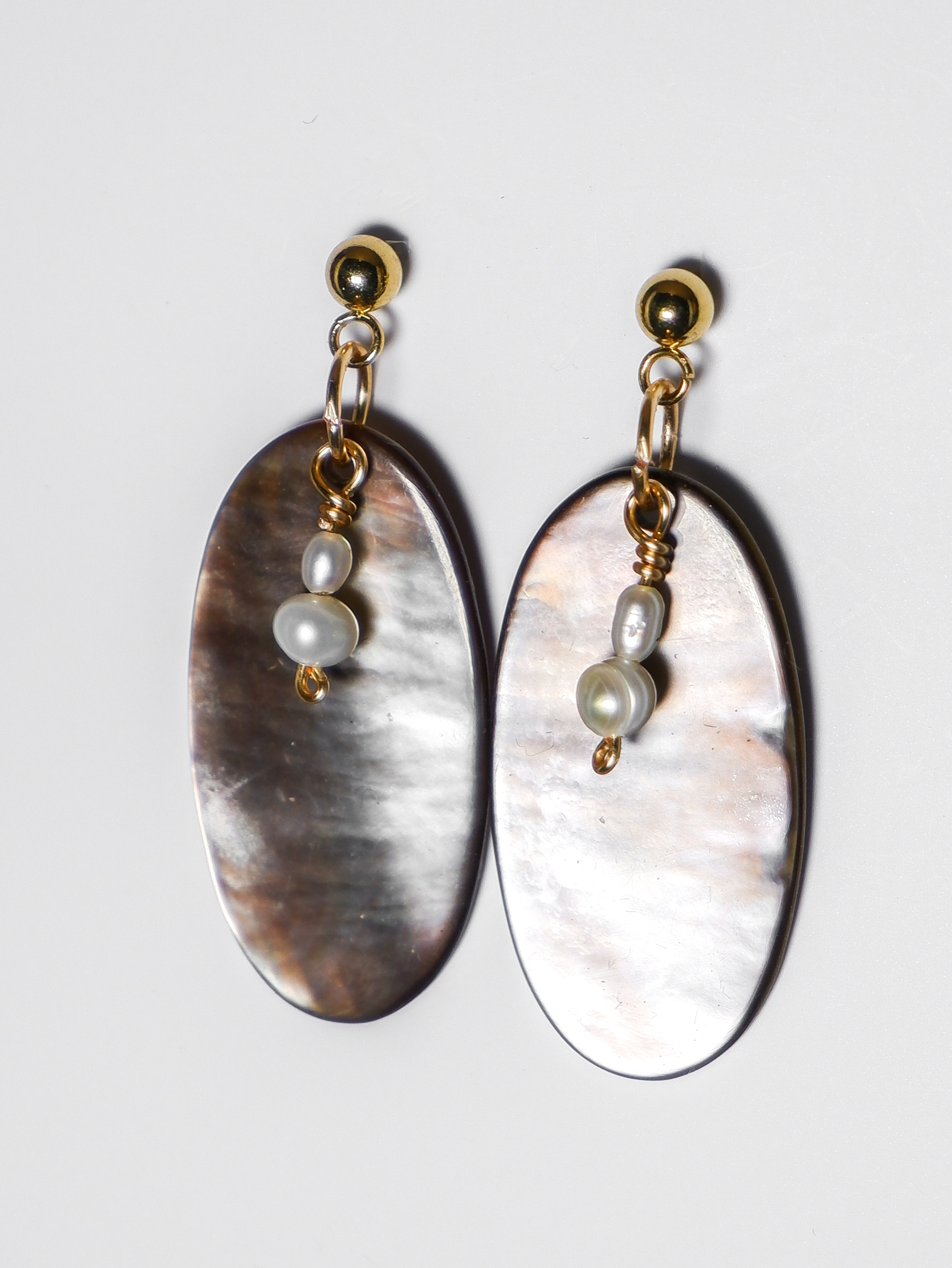 An ultra close-up shot of a gold earrings with pearl and an oval-shaped abalone mother of pearl on a white background.