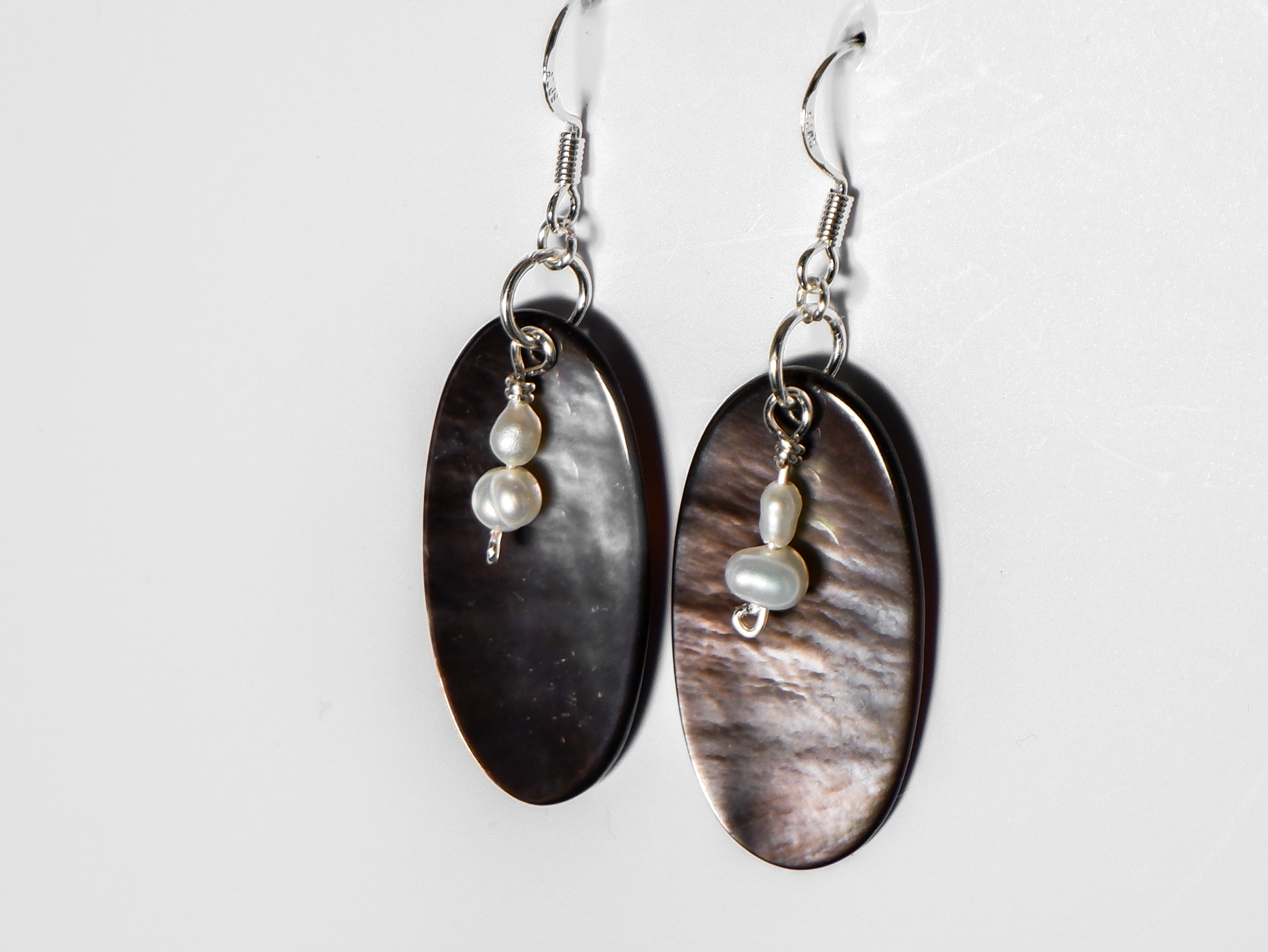 A close up shot of a silver earrings with pearl and an oval-shaped abalone mother of pearl on a white background.