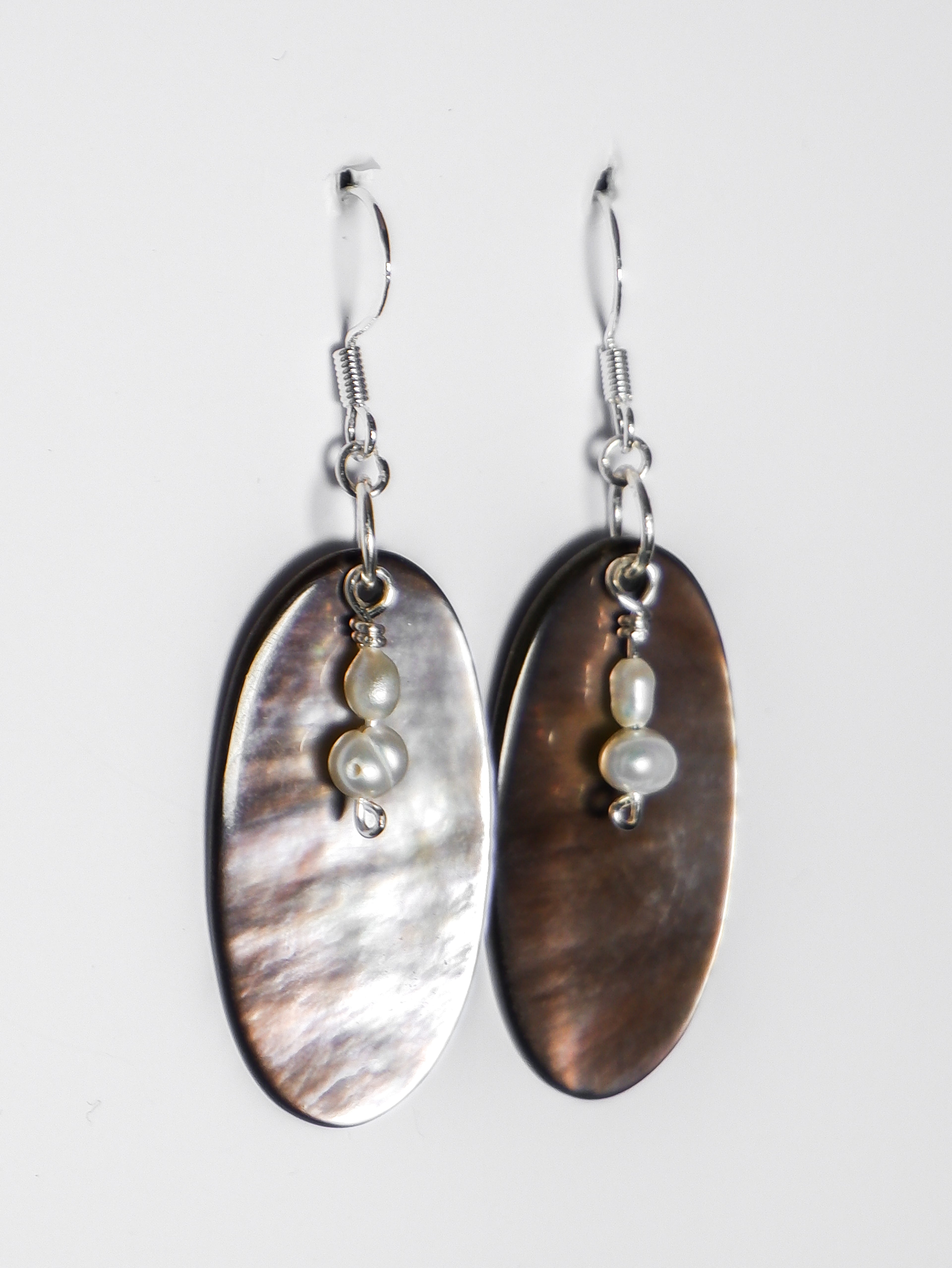 An ultra close-up shot of a silver earrings with pearl and an oval-shaped abalone mother of pearl on a white background.