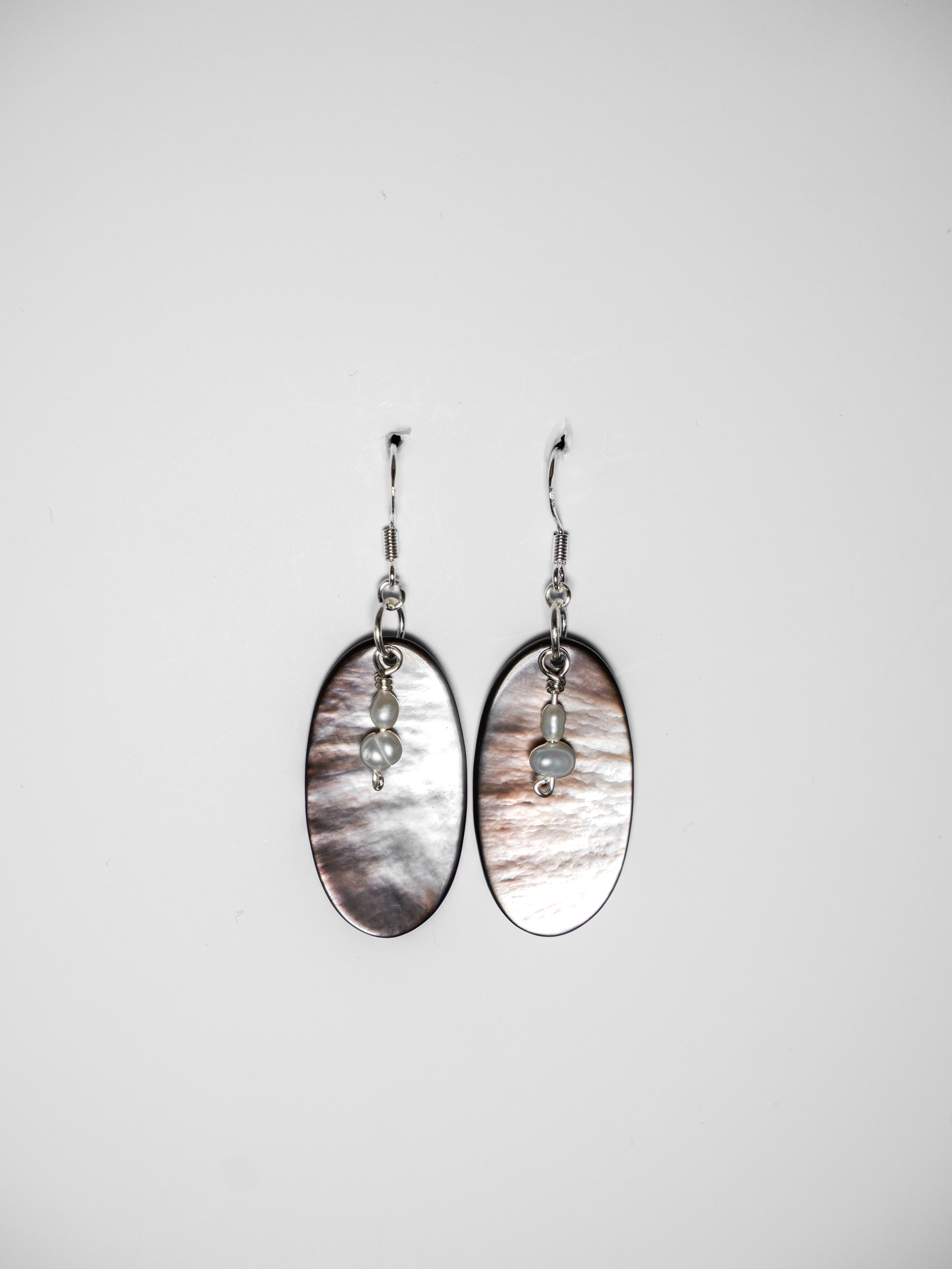 A wide-shot of a silver earrings with pearl and an oval-shaped abalone mother of pearl on a white background.