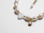 An ultra close-up shot of a gold pearl bracelet, with an off-centre heart-shaped mother of pearl and gold star charm lying on a white background.