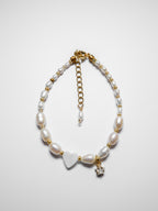 A gold pearl bracelet, with an off-centre heart-shaped mother of pearl and gold star charm on a white background.