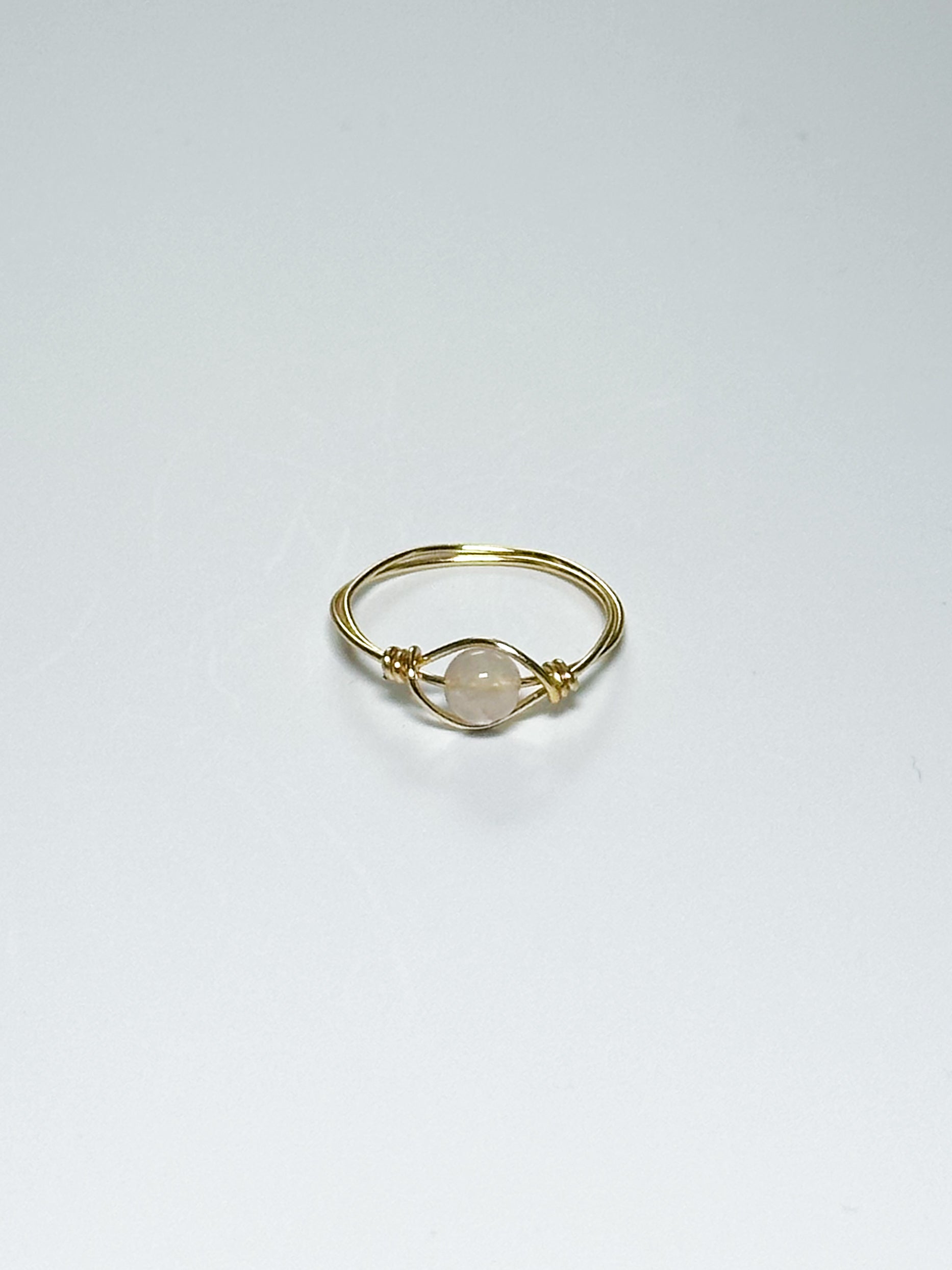 Gold ring with a light pink bead on an eye-like body on a white background with shadows.