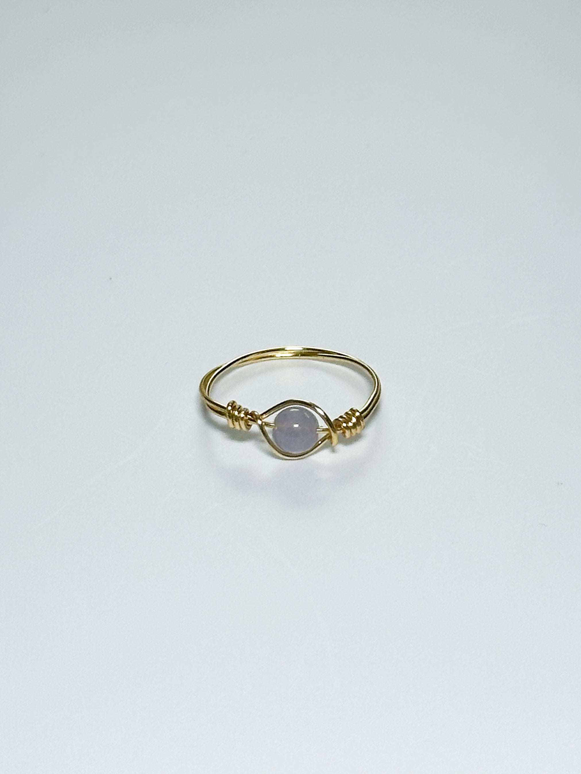 Gold ring with a light purple stone on an eye-like body on a white background with shadows.