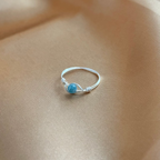 Silver wrapped ring with a blueish green stone on beige pink fabric background.